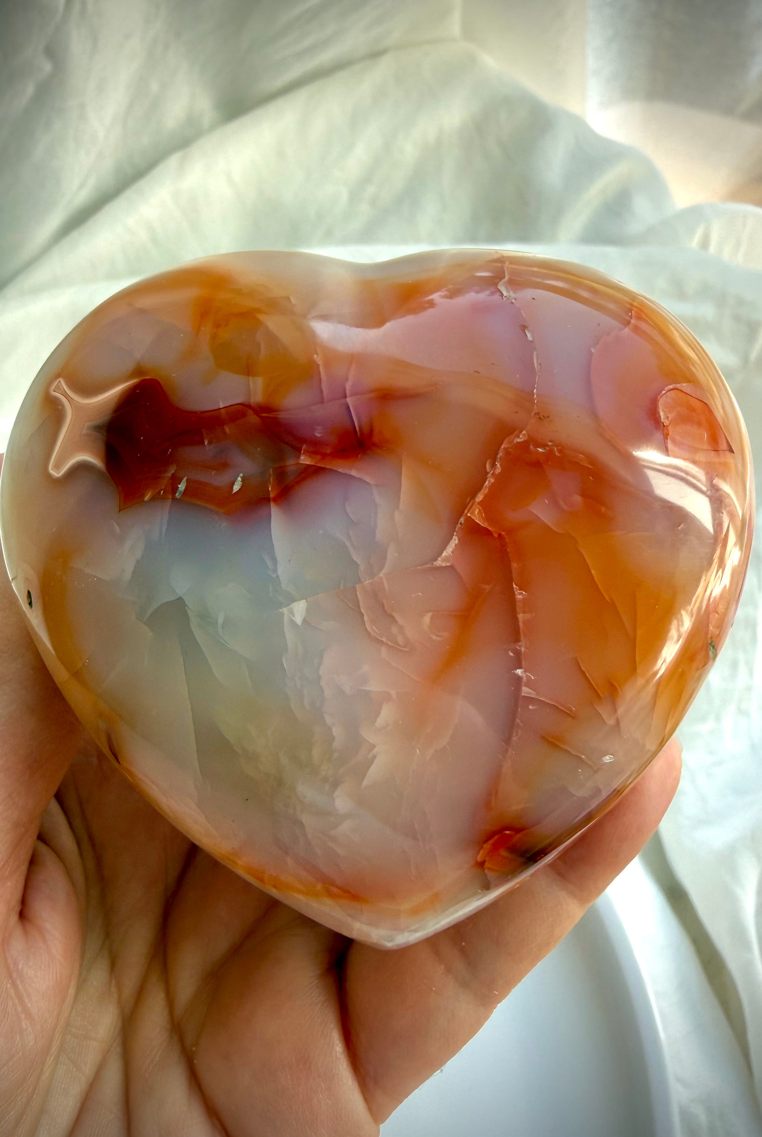 Polished Carnelian heart crystal held in hand for size reference showing natural orange colors and smooth heart shape