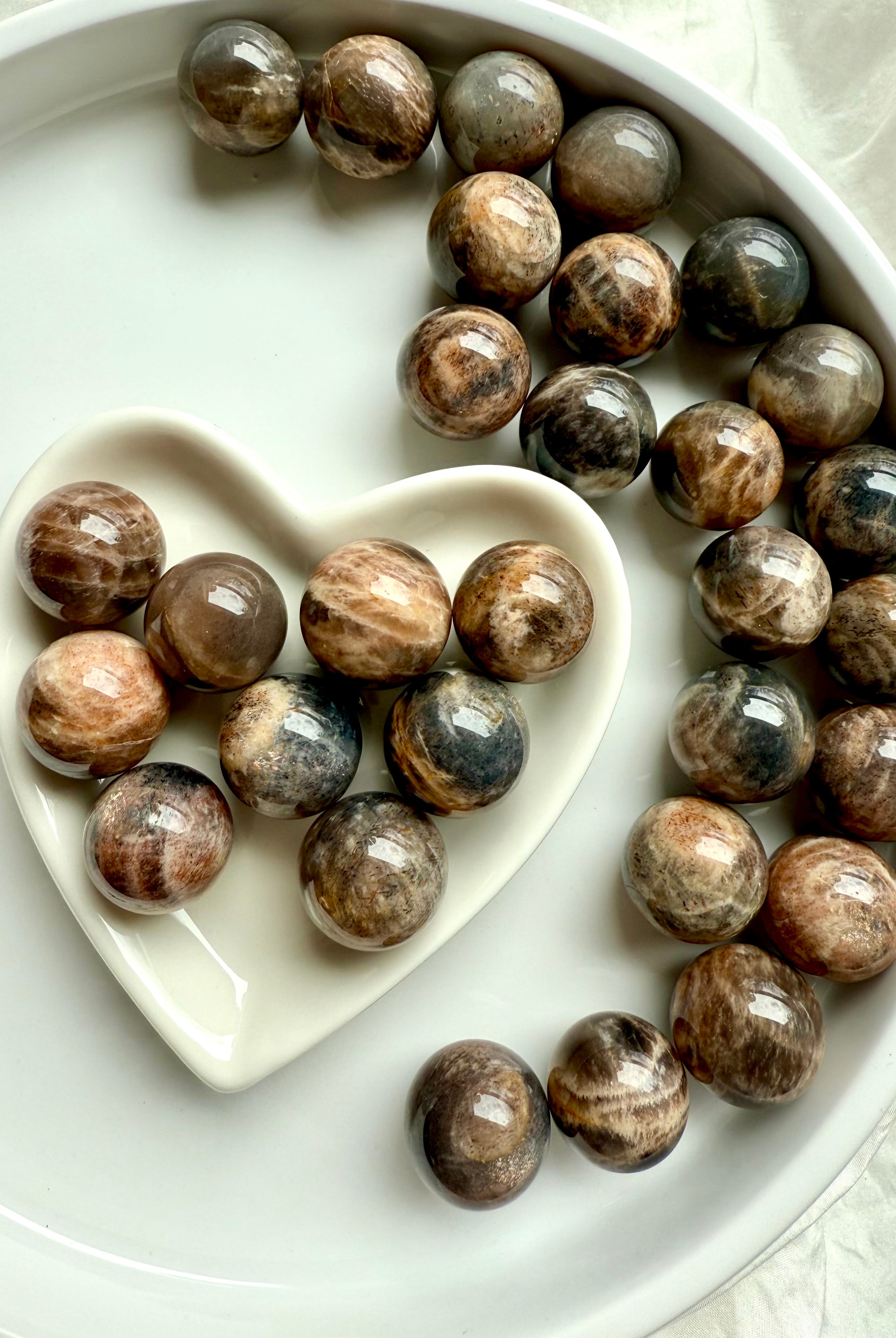 Grounding Mini Black Moonstone spheres with Sunstone shimmer in a white heart-shaped bowl for intuition