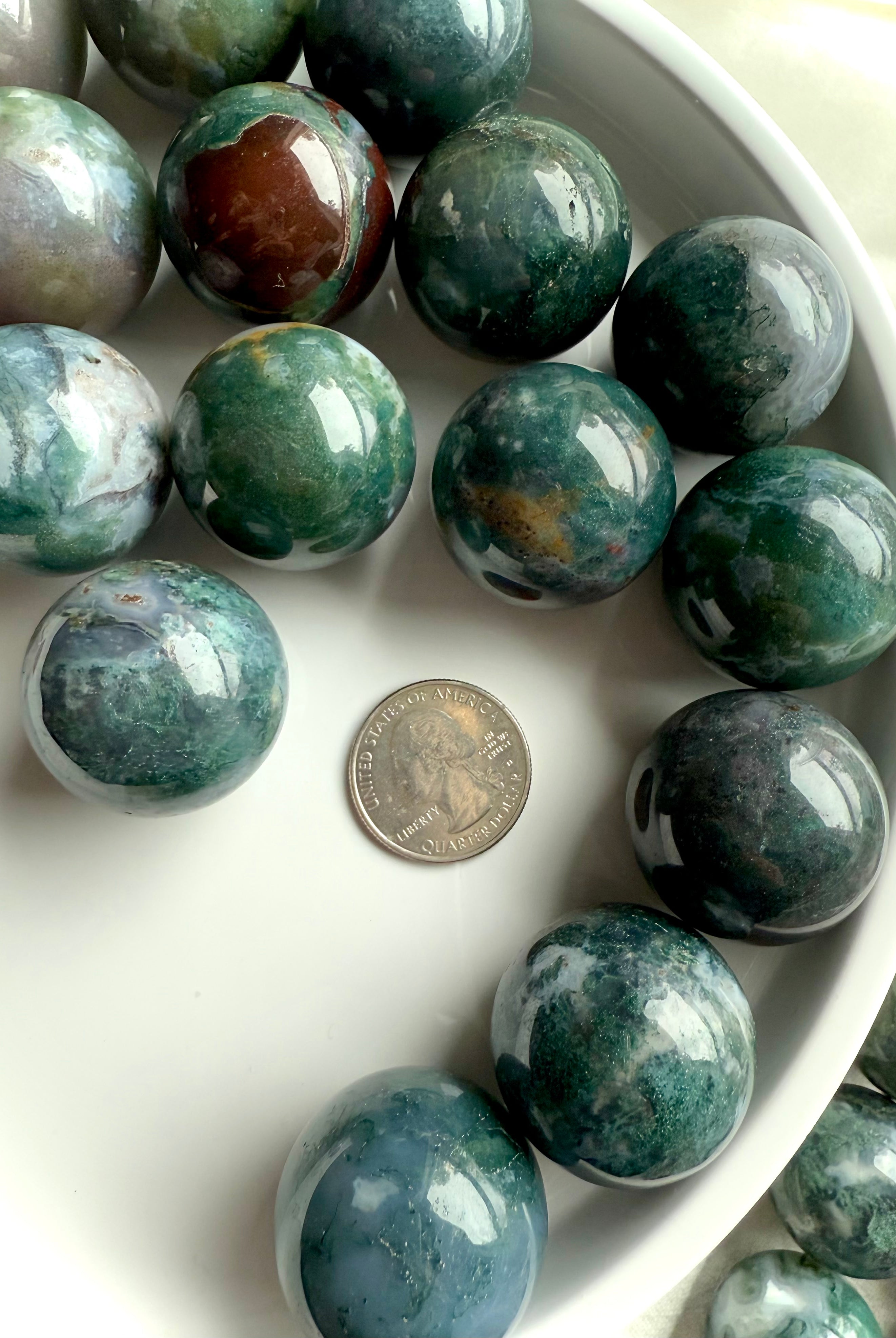Colorful moss agate mini spheres shown on a white plate with a quarter for scale