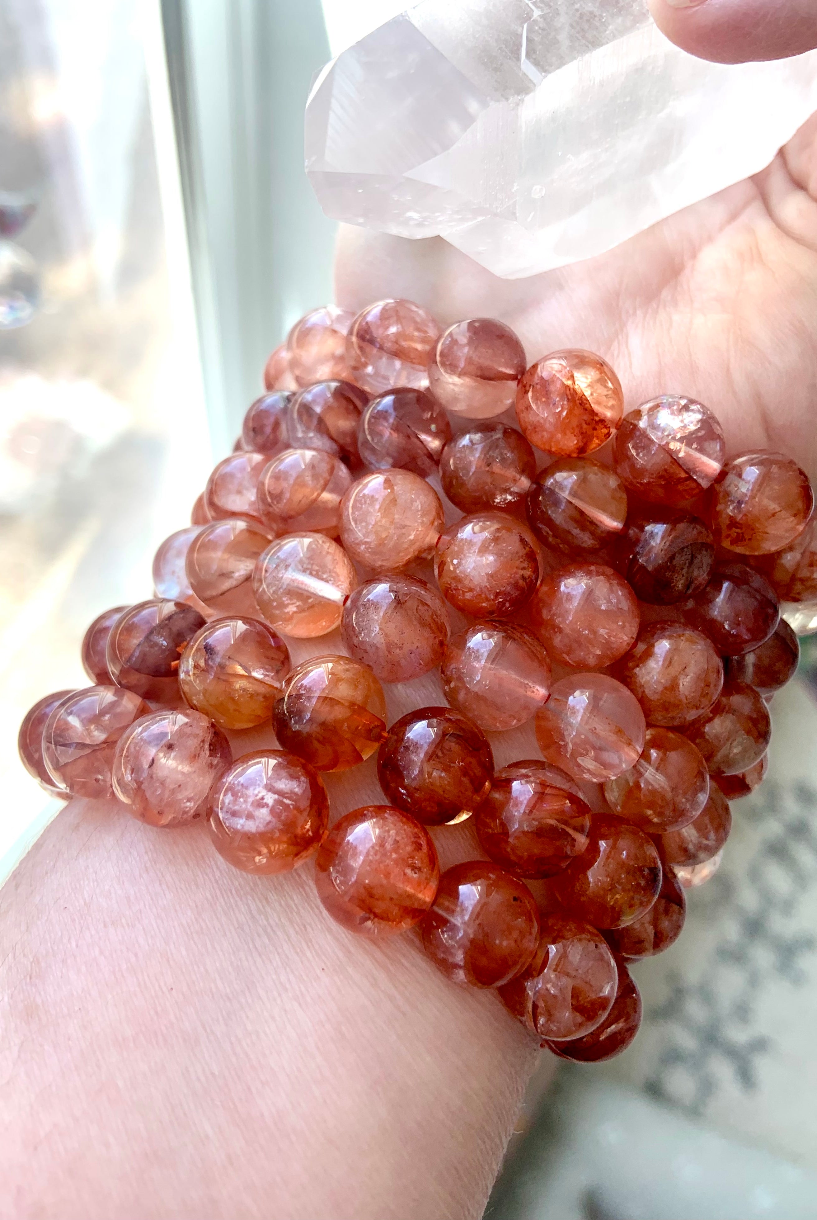 Stack of large Fire Quartz bracelets worn on wrist while holding a clear quartz crystal, showing vibrant energy and bold 11.2–11.8mm beads