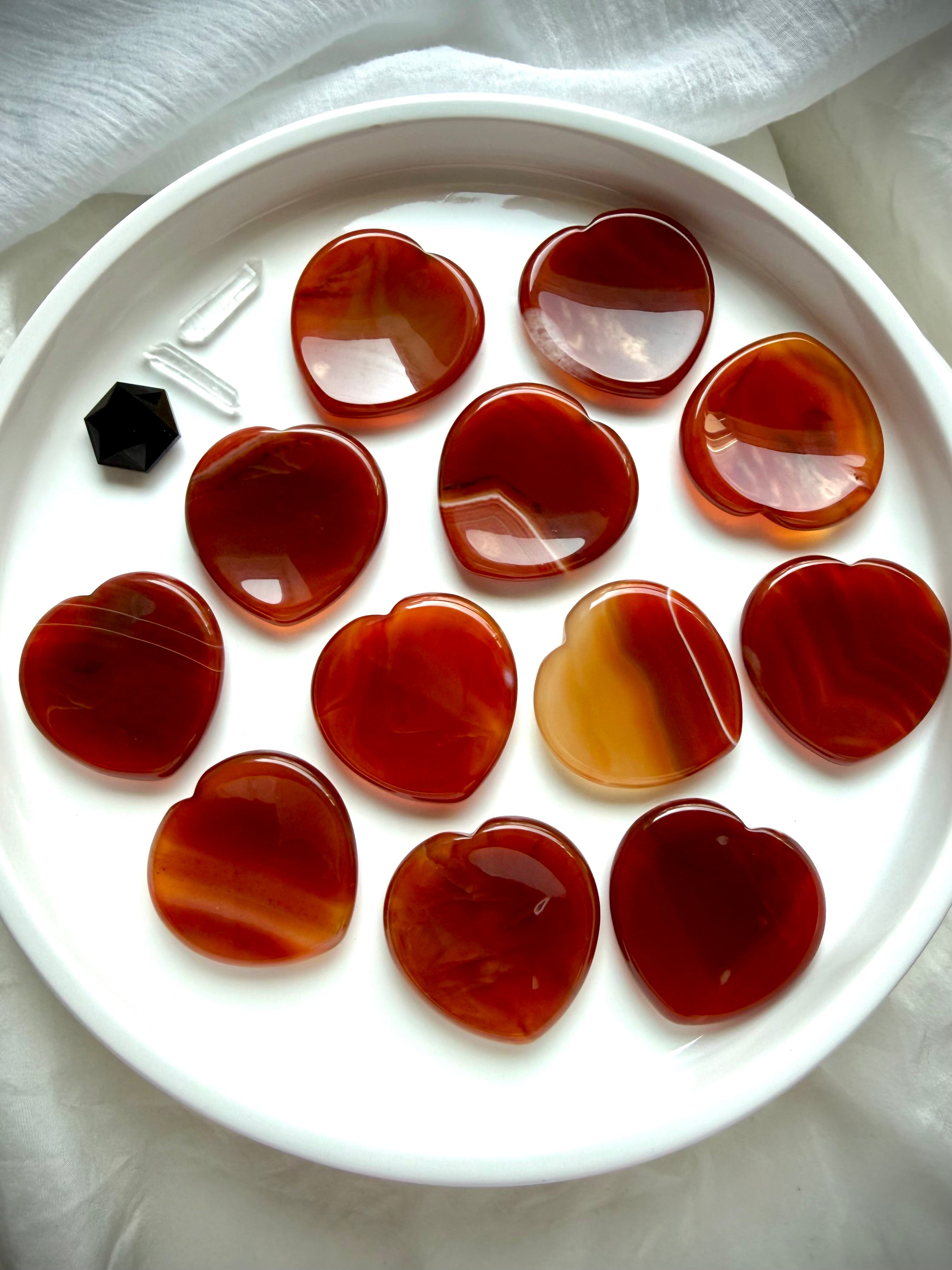 Carnelian heart worry stones on white tray showing natural red, orange, amber and golden color variation