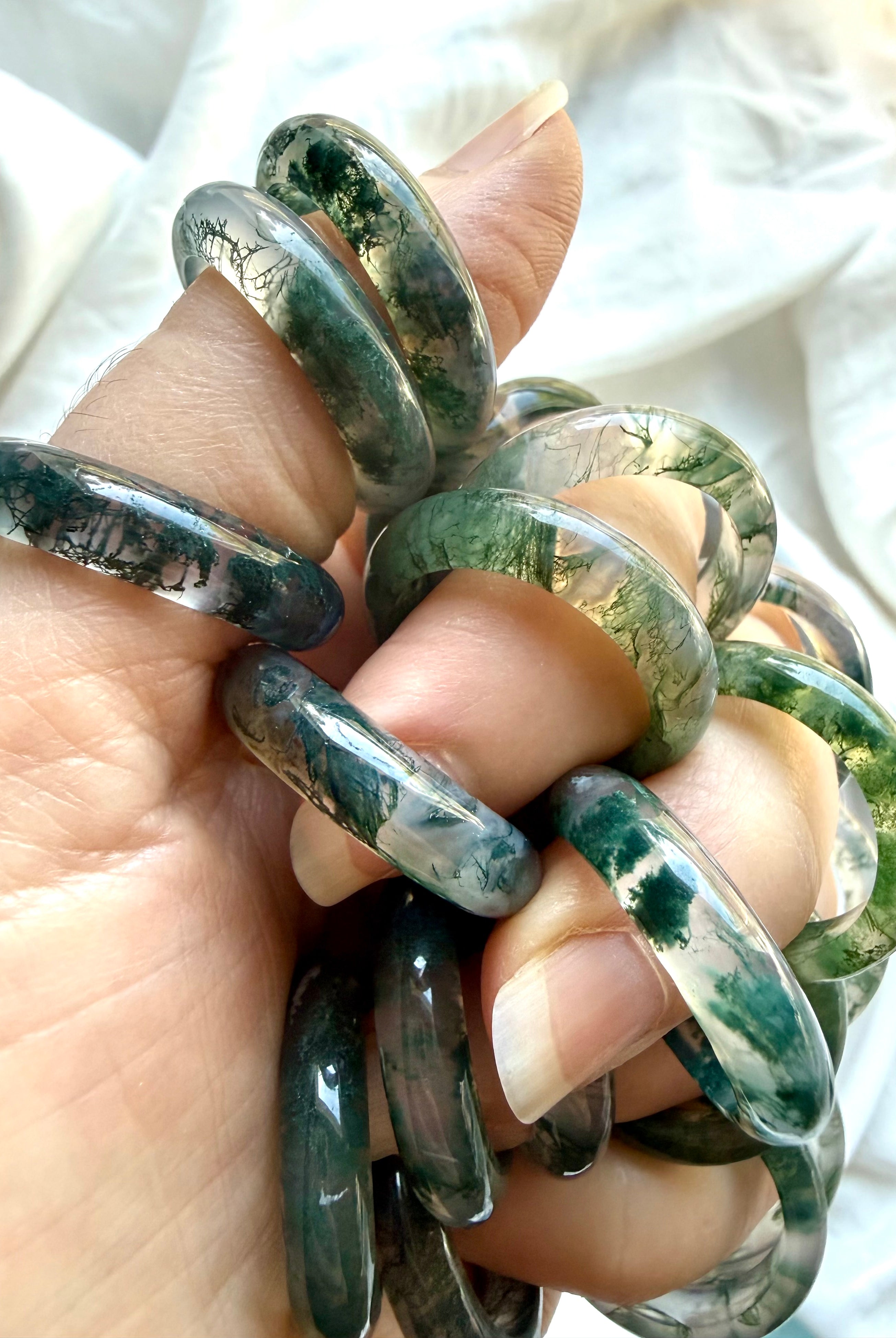 hand holding moss agate band rings showing natural inclusions and polished finish, translucent crystal ring for calm balance and renewal