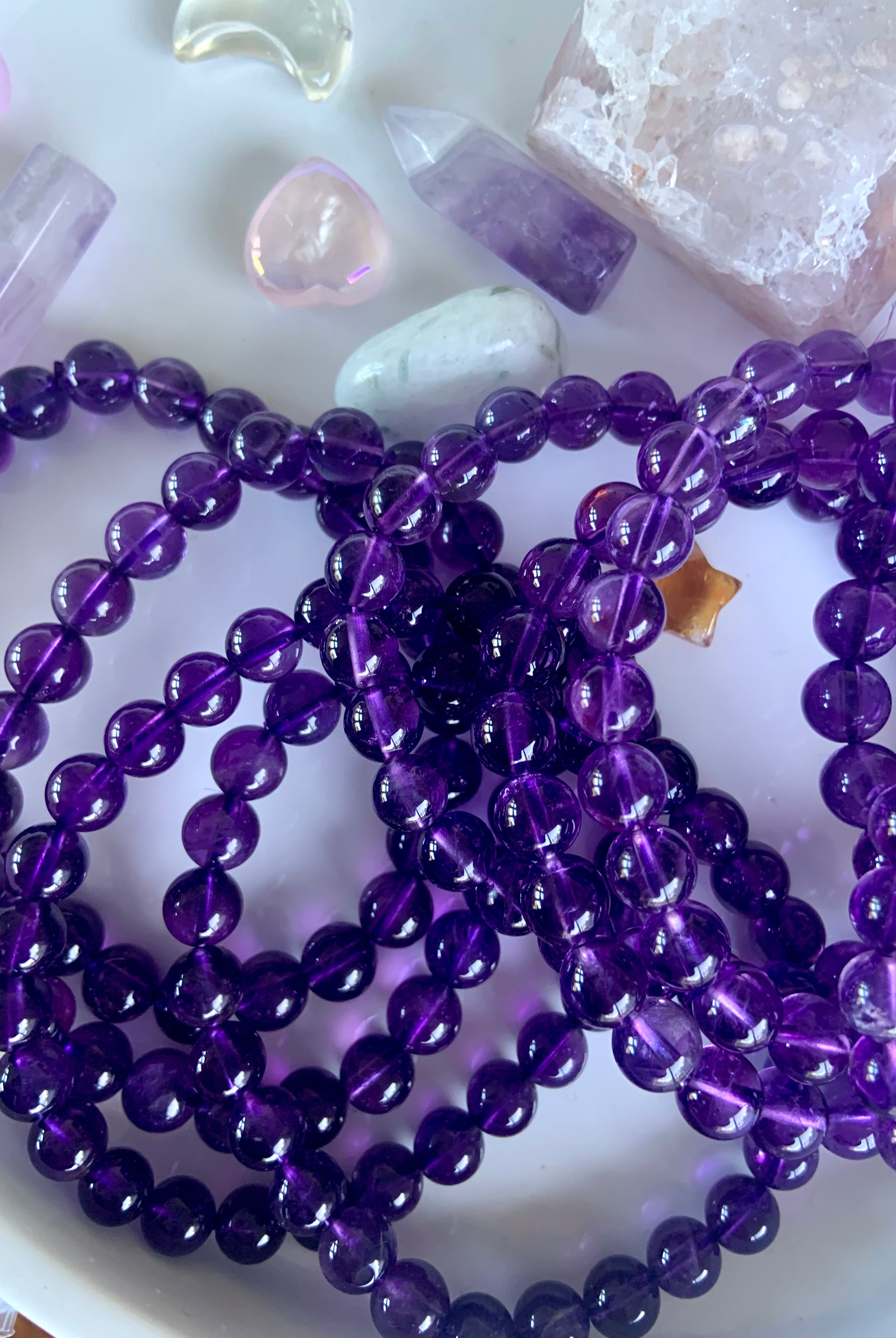 Overhead view of deep purple amethyst crystal bead bracelets on a white plate with mini crystals in the background