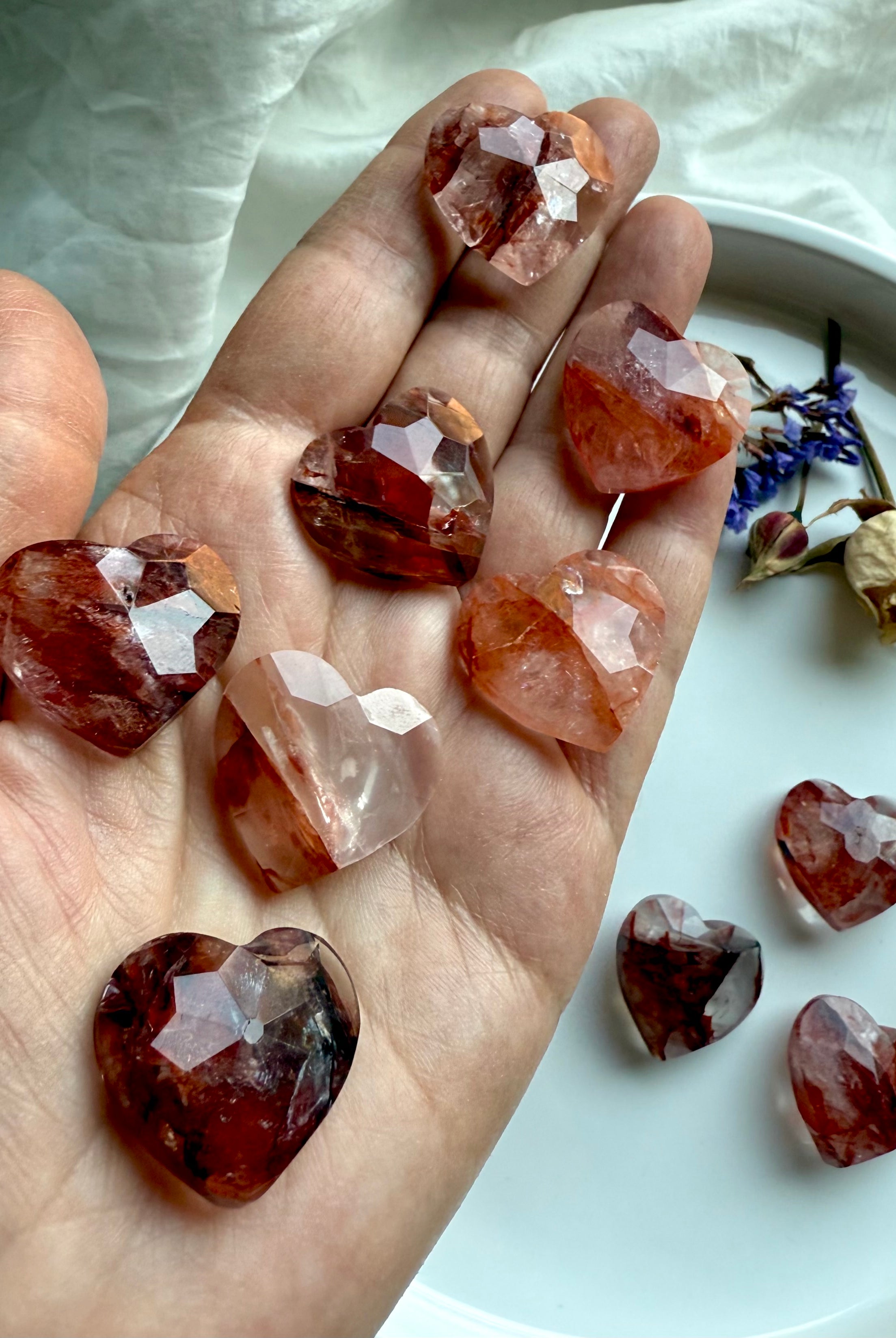 Array of faceted Fire Quartz mini crystal hearts displayed on hand – natural healing stones for grounding, balance, and spiritual support
