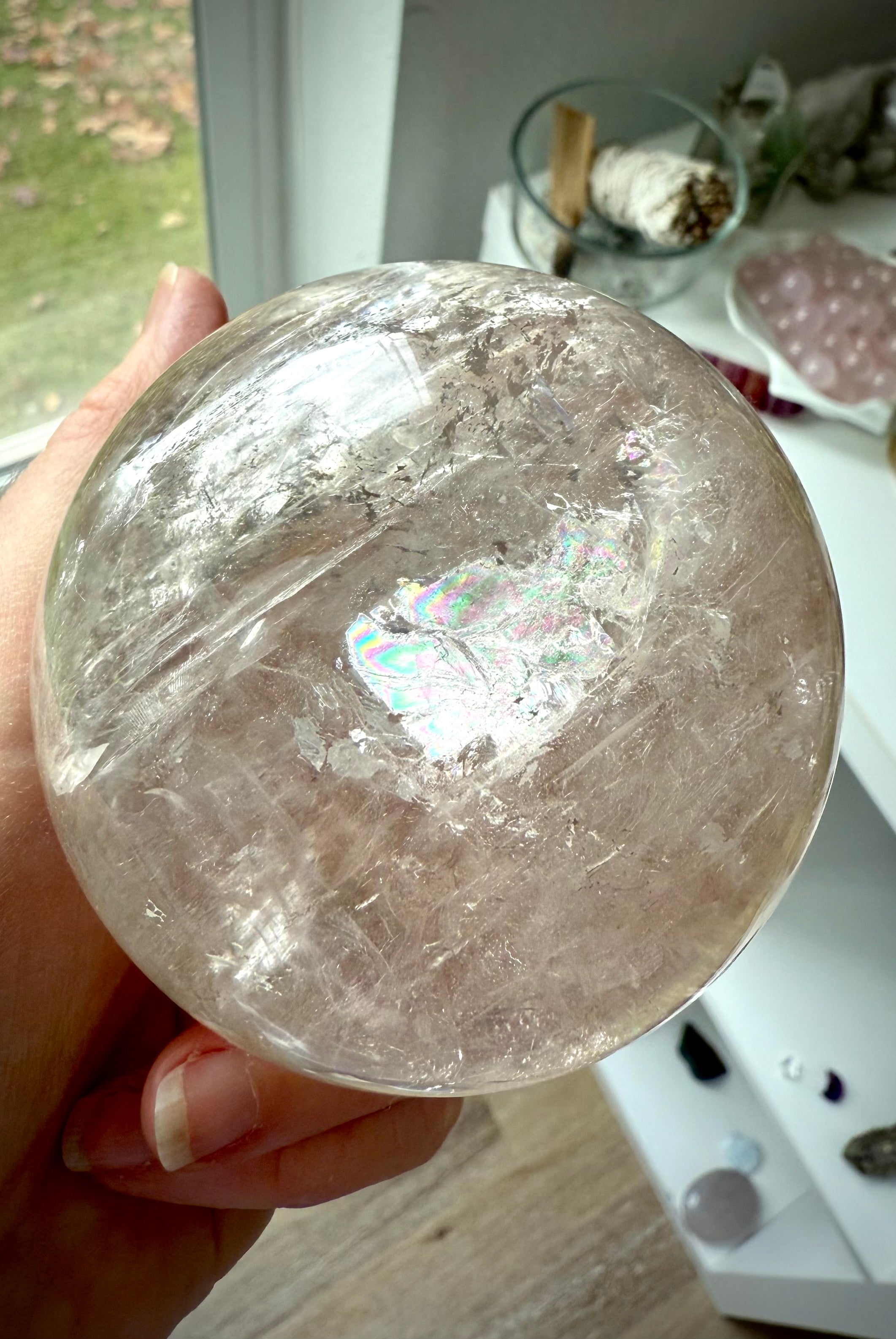 A hand holding a Champagne Smokey Quartz Sphere with visible silver flash and rainbow inclusions.