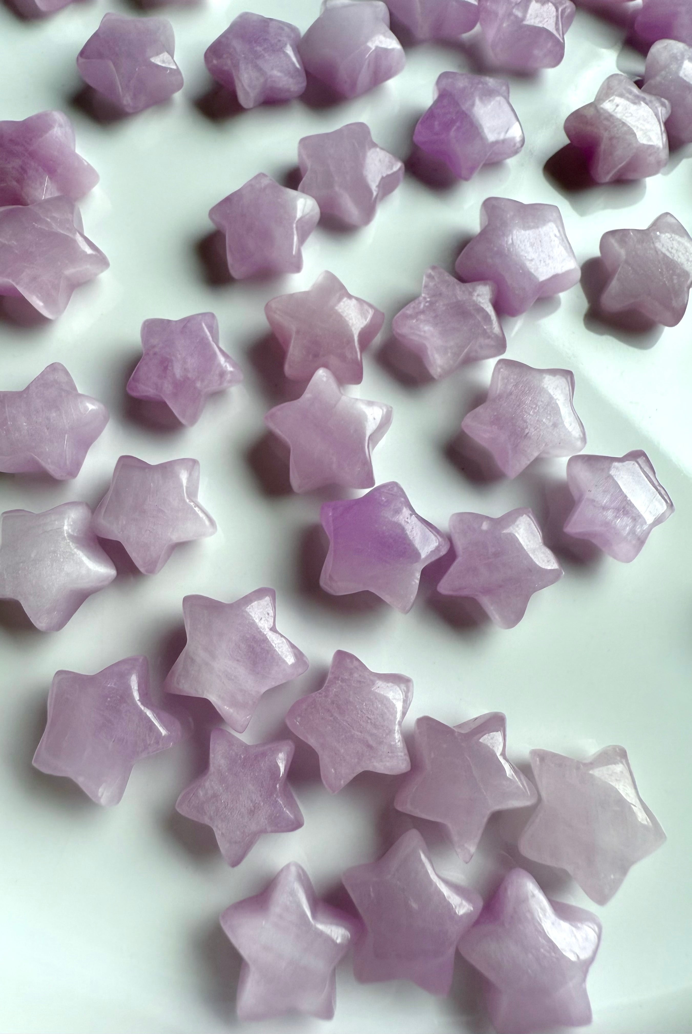 Kunzite mini star carvings on white background – tiny heart chakra crystals in pale pink and lilac hues with glossy polish and soft shimmer.