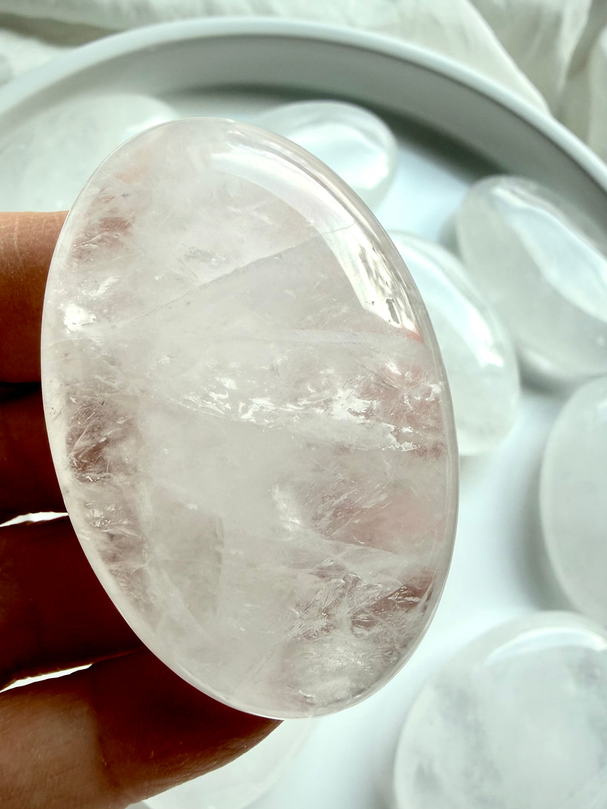 Polished Clear Quartz palm stone held in hand with white crystalline patterns, silvery flashes and translucent clarity