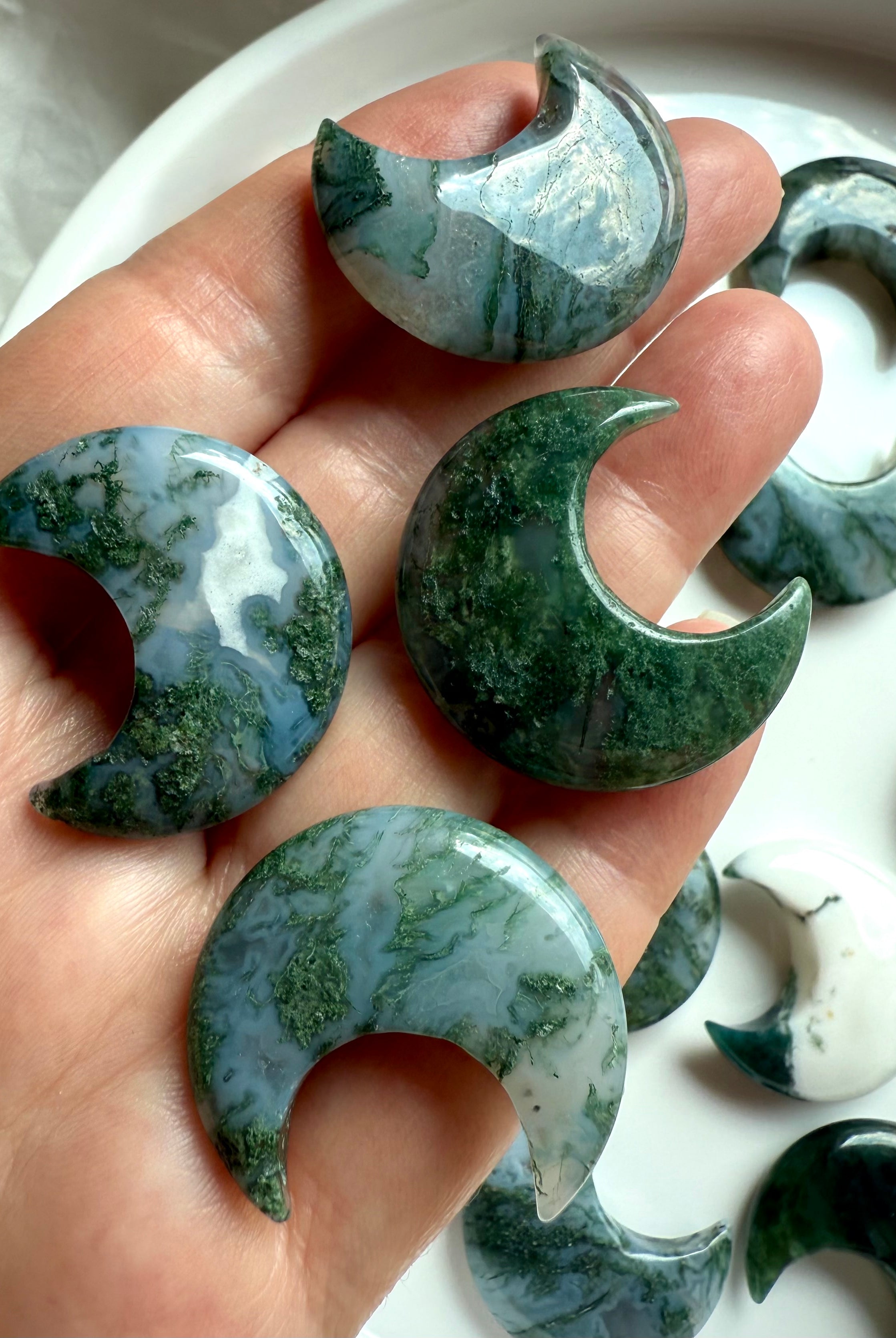 Close-up of four Moss Agate crescent moon crystals in hand showing variation in color, pattern, and translucence.