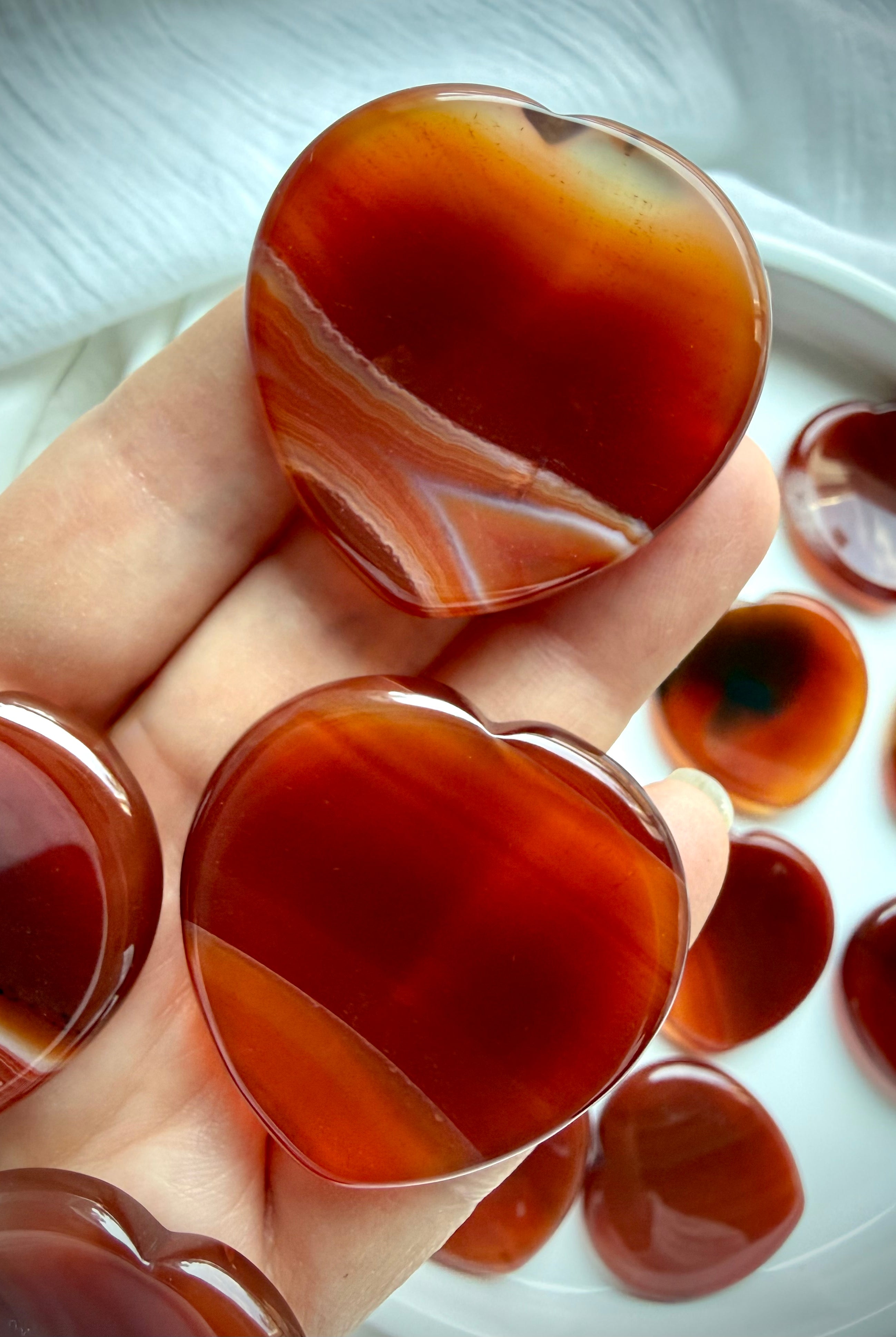 Carnelian heart worry stones held in hand with rich red-orange tones, natural banding and smooth thumb indentations