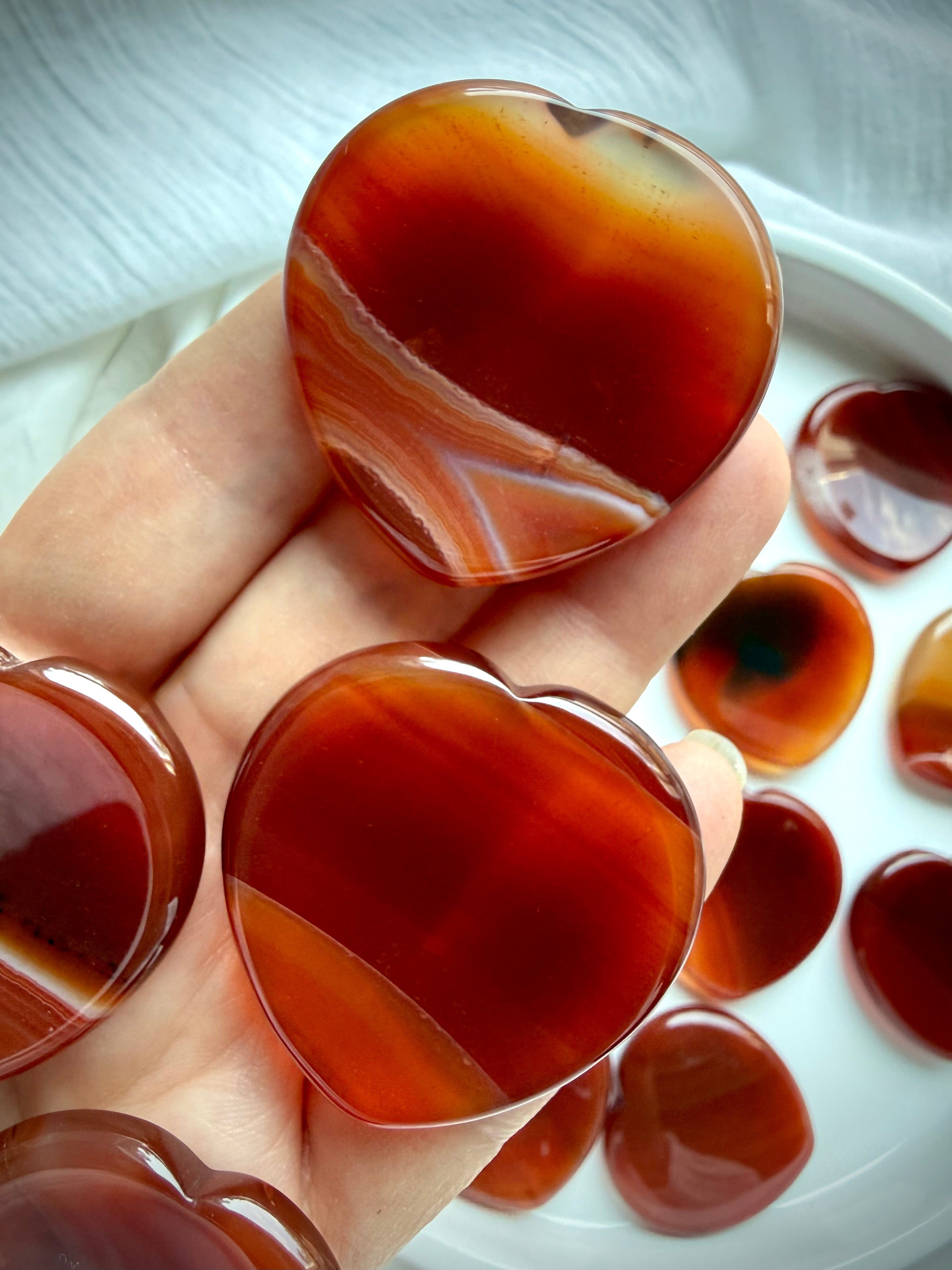 Carnelian heart worry stones held in hand with rich red-orange tones, natural banding and smooth thumb indentations