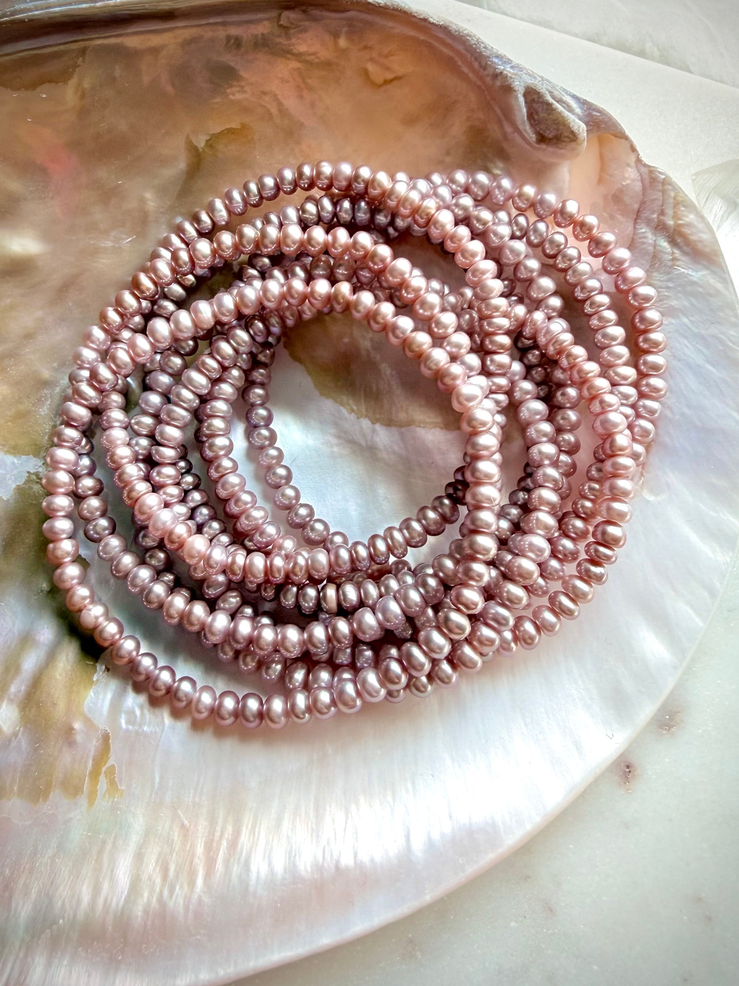 coiled pink freshwater pearl bracelets arranged together on a shell, soft pink pearl jewelry stack with luminous sheen