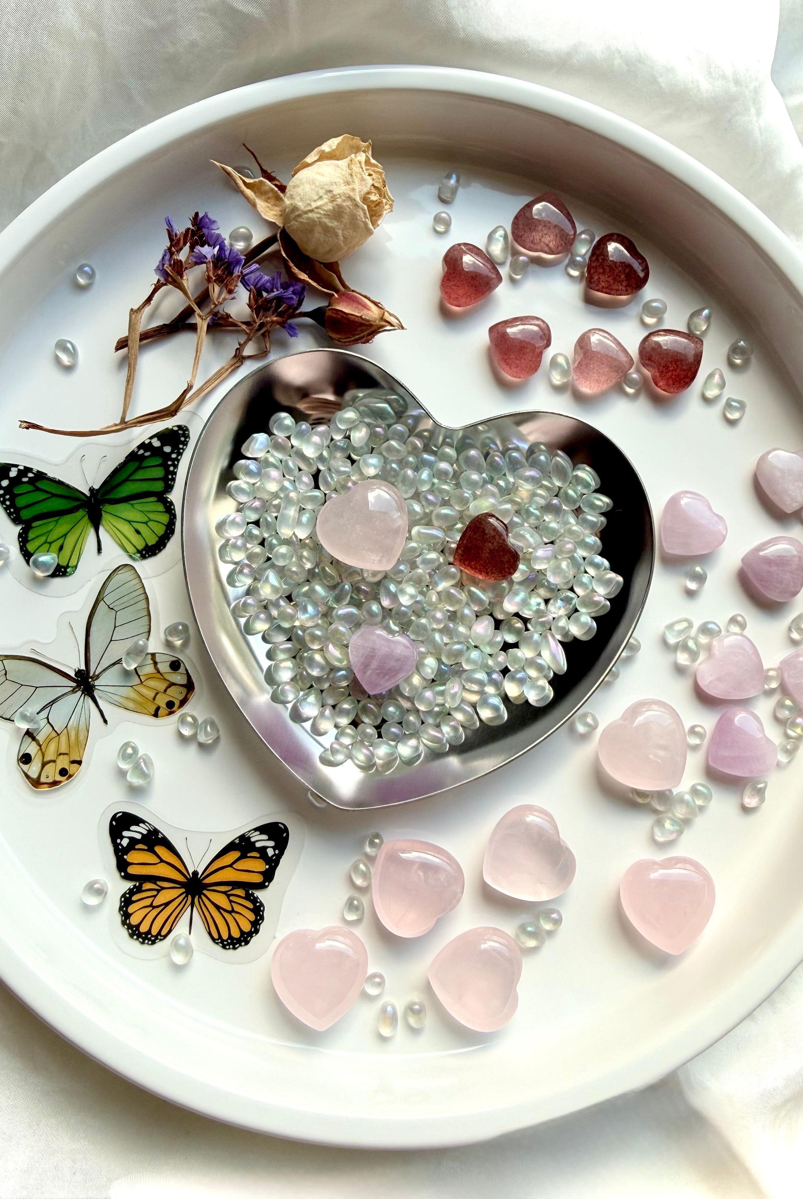 Array of crystal heart sets styled with rose quartz, strawberry quartz, and kunzite mini heart carvings surrounded by aura crystal confetti and butterfly accents
