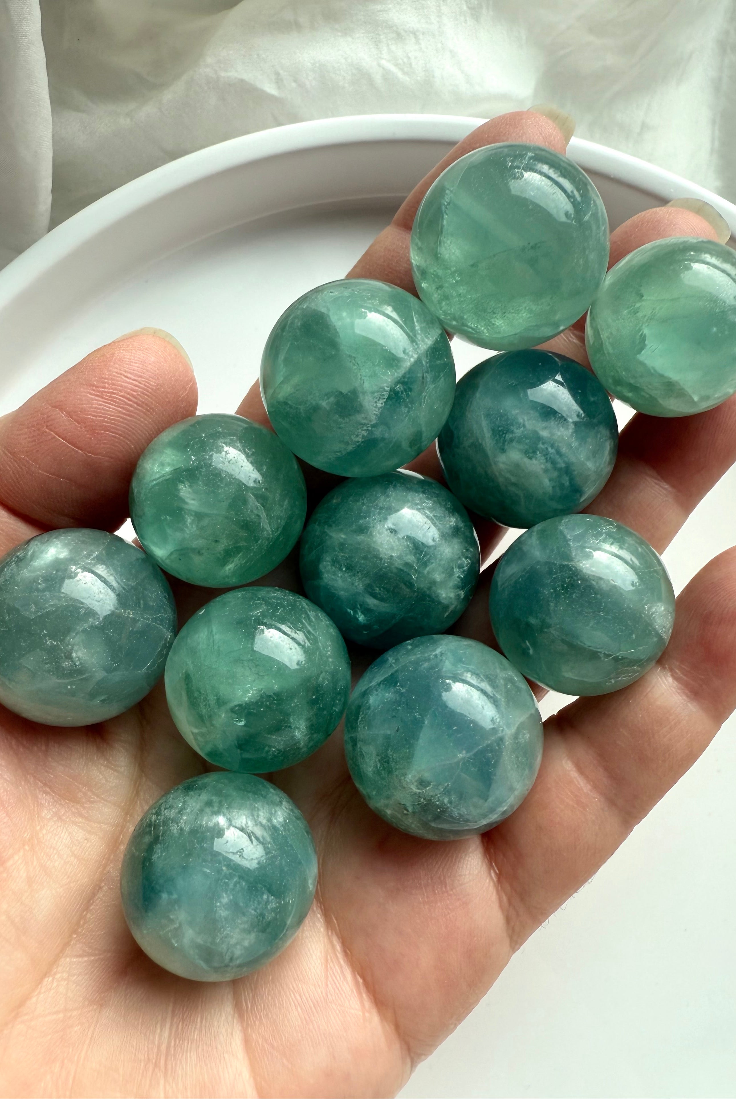 Hand holding several teal Fluorite mini spheres, soothing aqua green crystal balls for focus and balance.