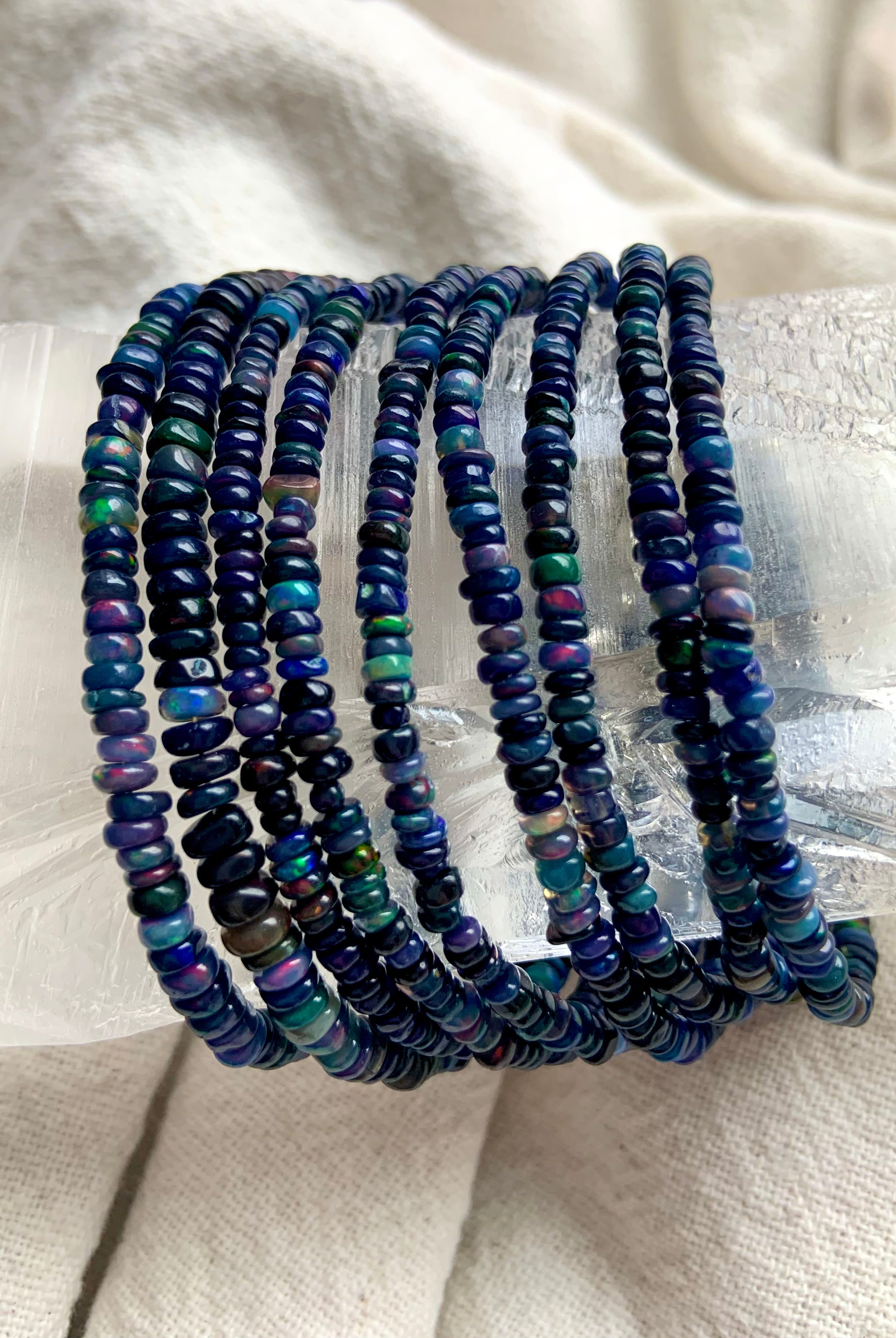 Black Fire Opal bracelets draped over a large clear quartz point — shimmering Ethiopian opal jewelry for October birthdays.
