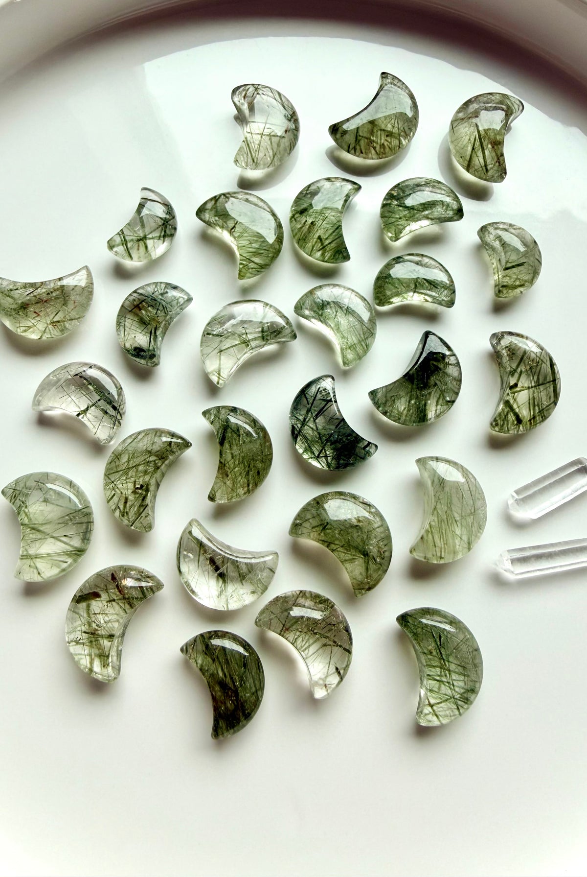 Green Tourmaline in Quartz moons on a white plate, green crystal carvings for Heart Chakra energy and abundance