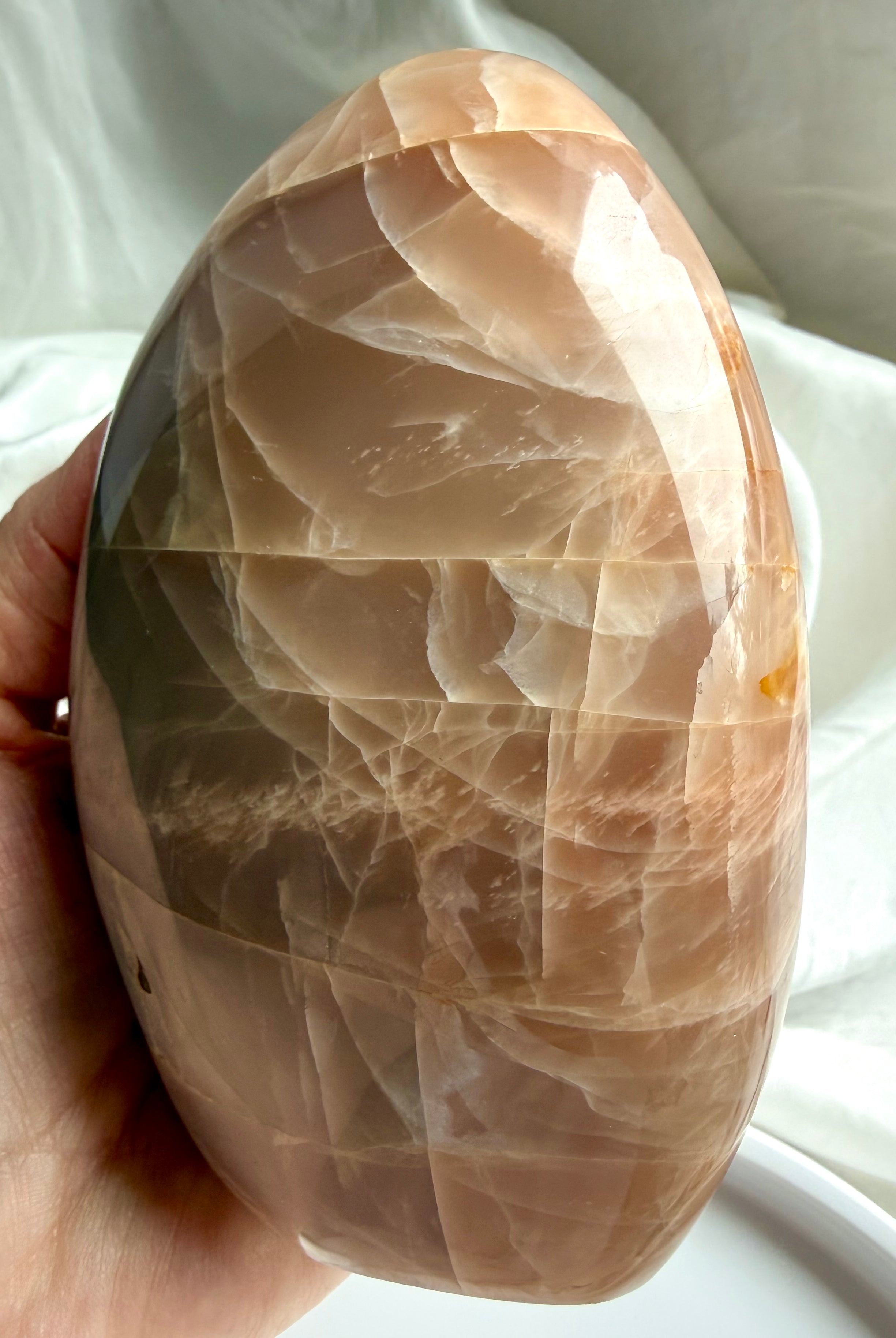Peach Moonstone freeform crystal with luminous flash and polished surface shown in natural sunlight