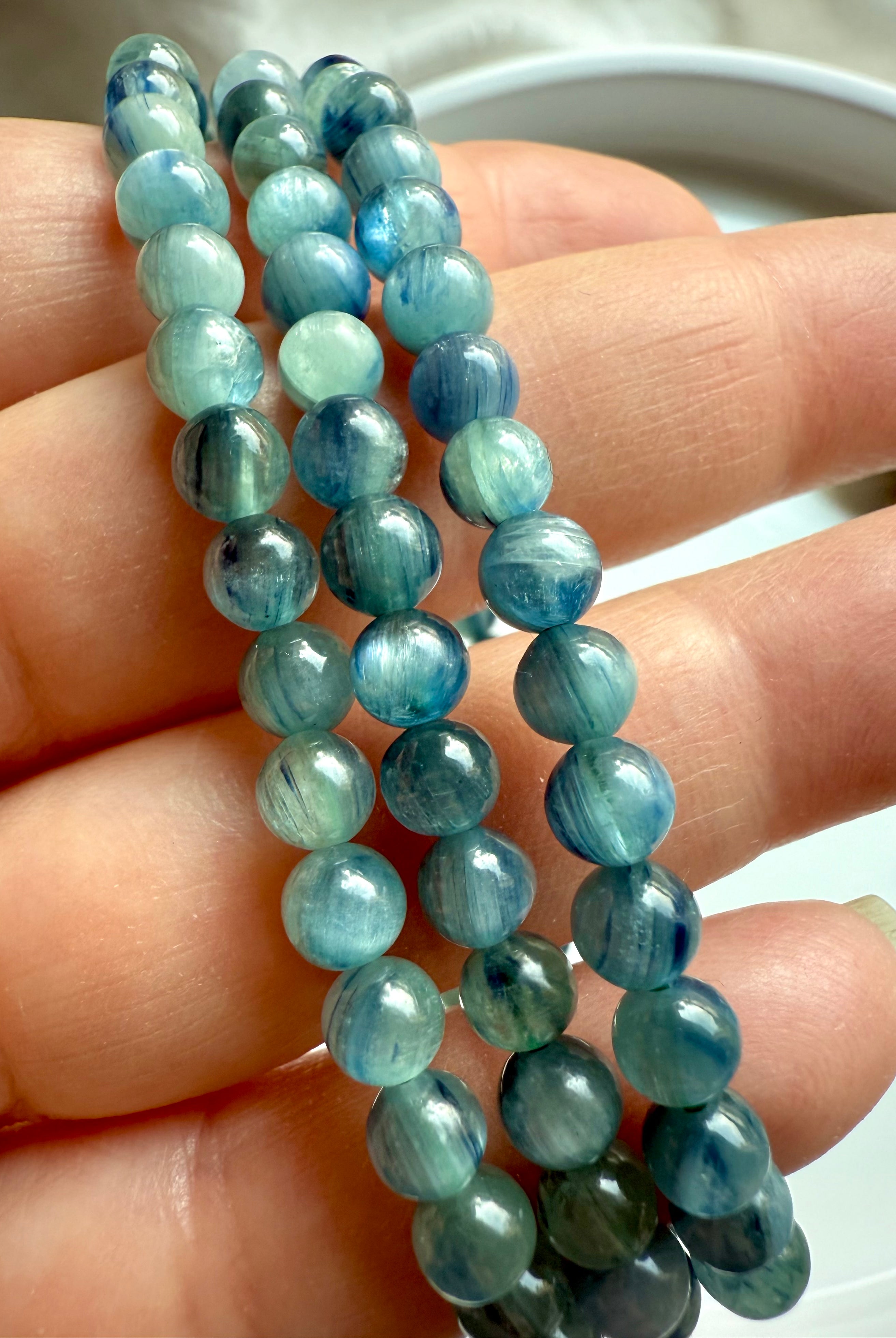 three polished kyanite bracelets in hand revealing fibrous gemstone texture and color variation in calming blue-green tones
