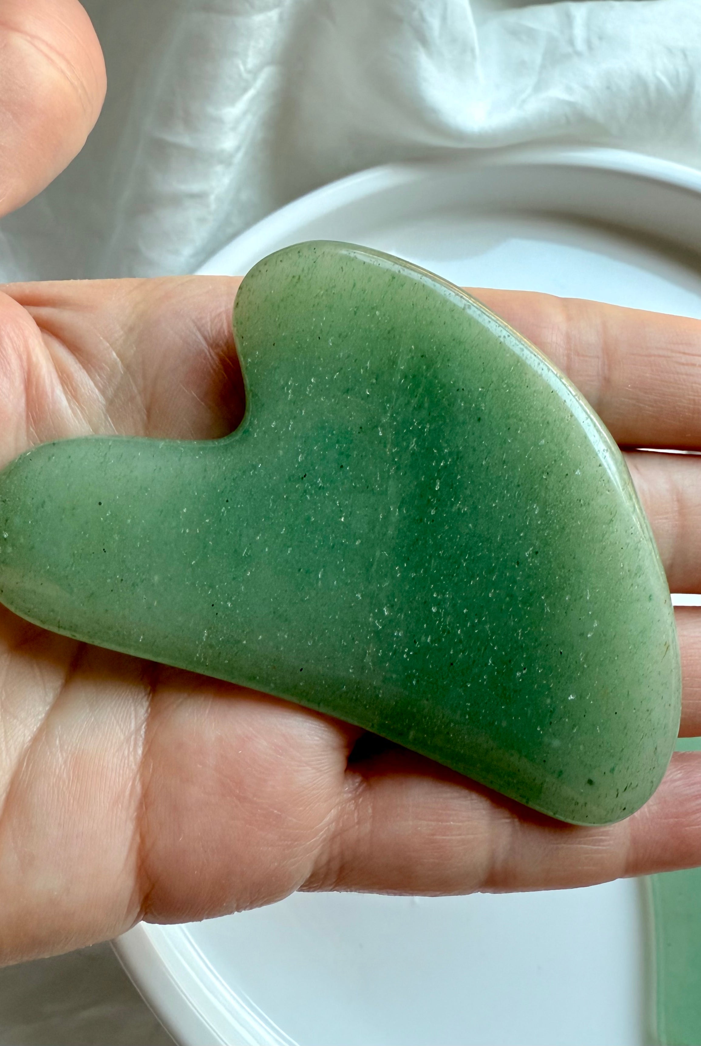 Close-up of Green Aventurine crystal gua sha facial massage tool resting in hand