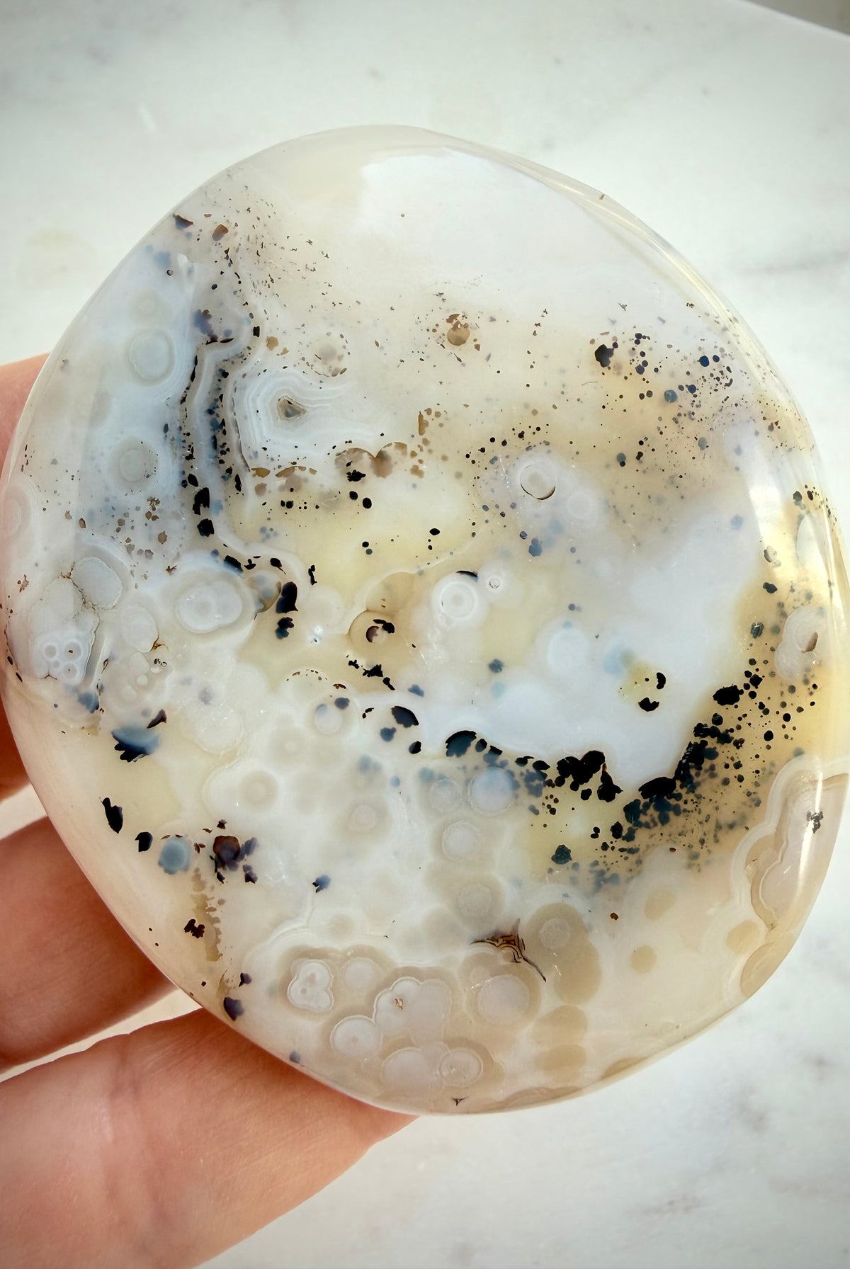 Natural Dendritic Agate freeform held in hand, showing delicate black dendrites and pale golden mineral inclusions