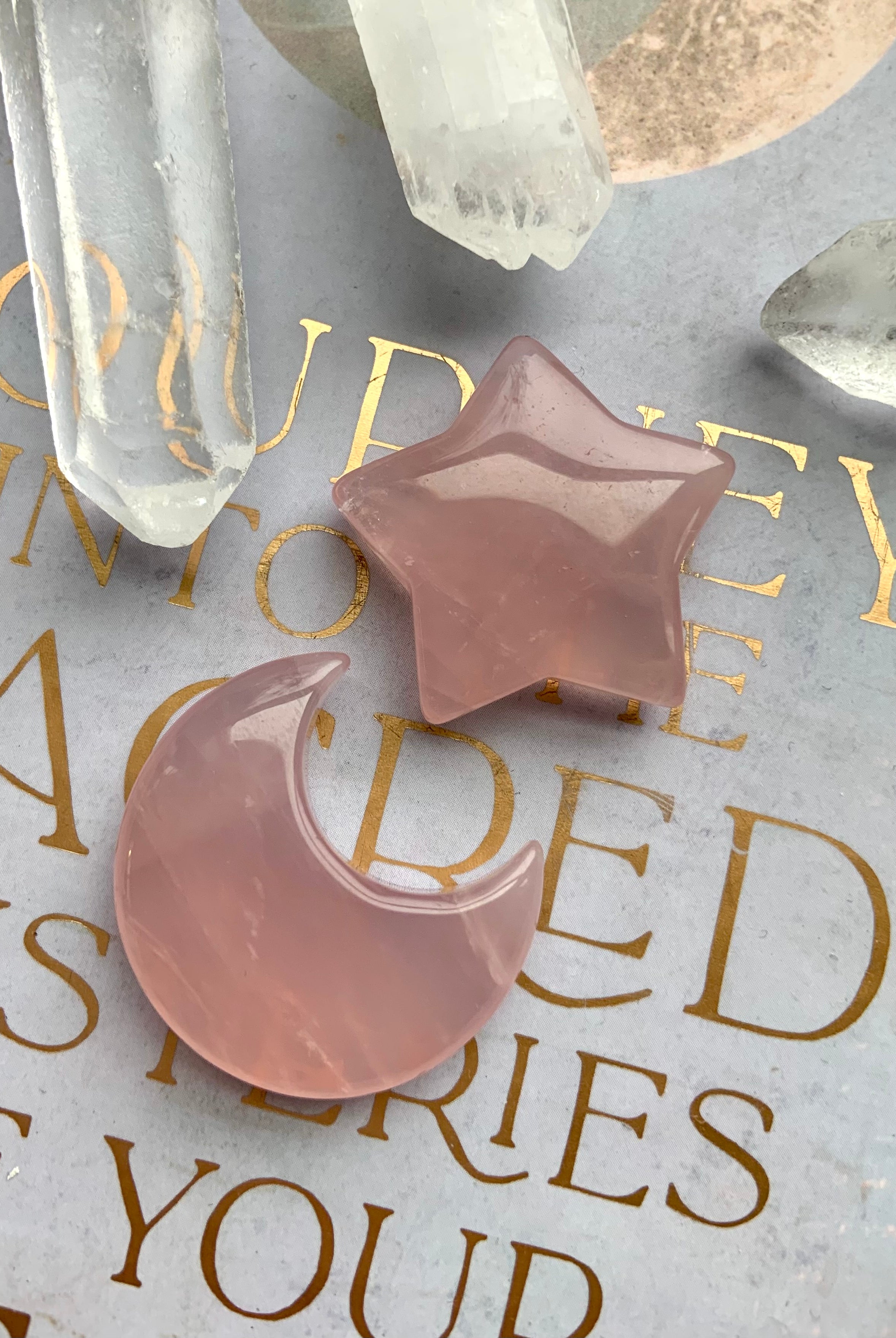 Closeup of rose quartz moon and star crystals with quartz points, styled on a lilac journal with gold text. Heart Chakra crystals of unconditional love.