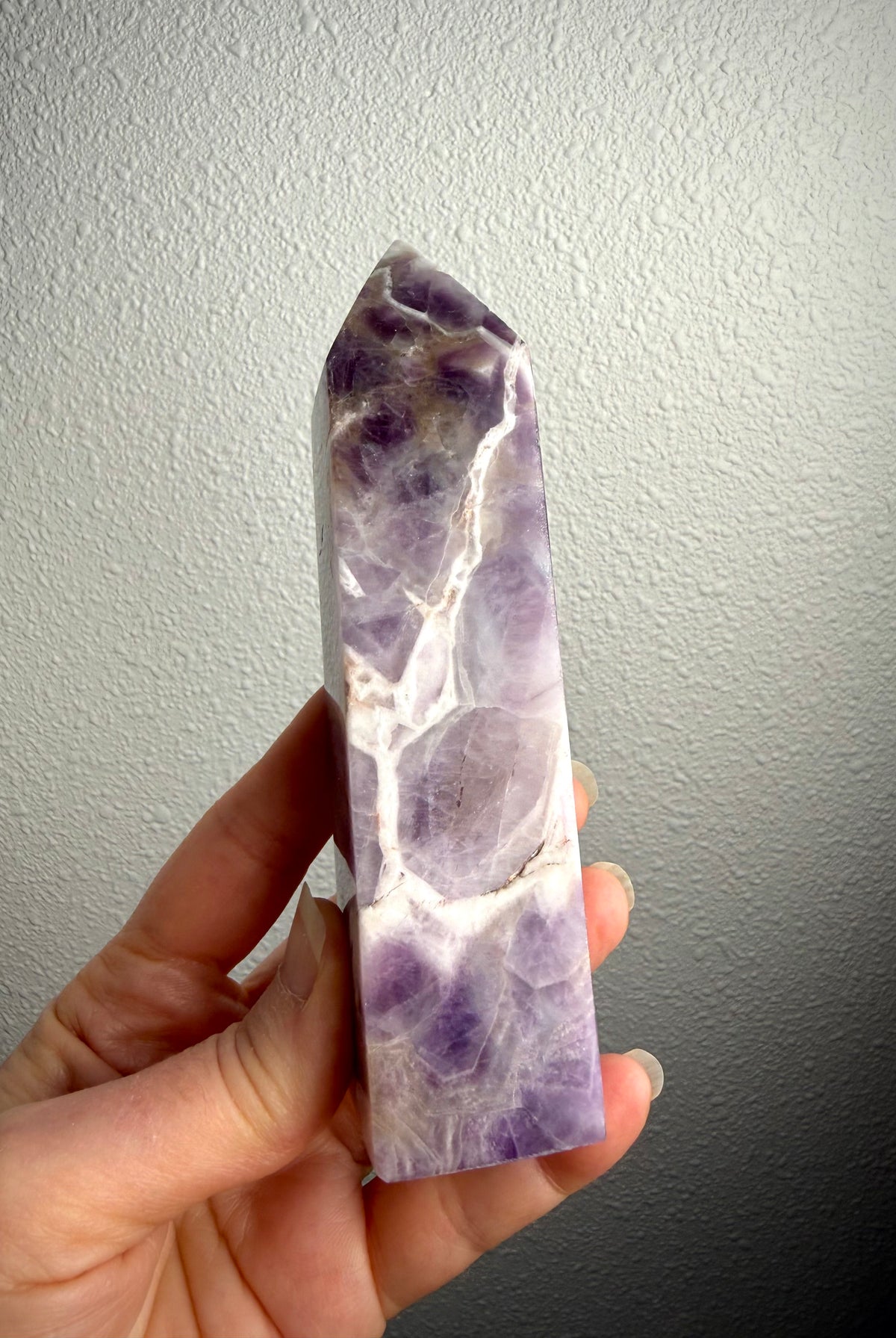 Dream Amethyst crystal point held in hand, showing its slender profile, lavender coloring and distinctive white quartz banding