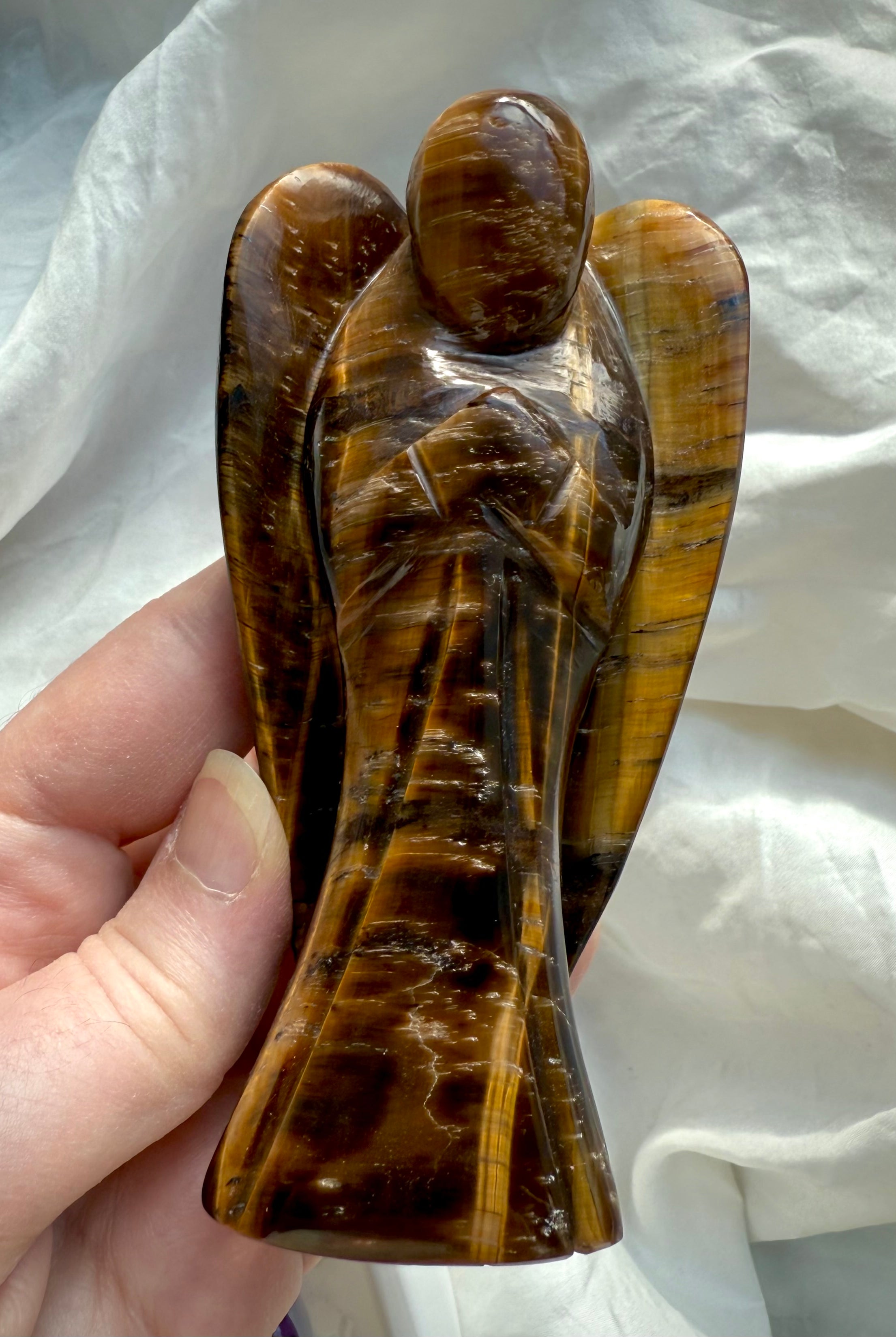 Hand holding Tiger’s Eye angel figurine with strong contrast in golden brown hues, emphasizing its guardian shape