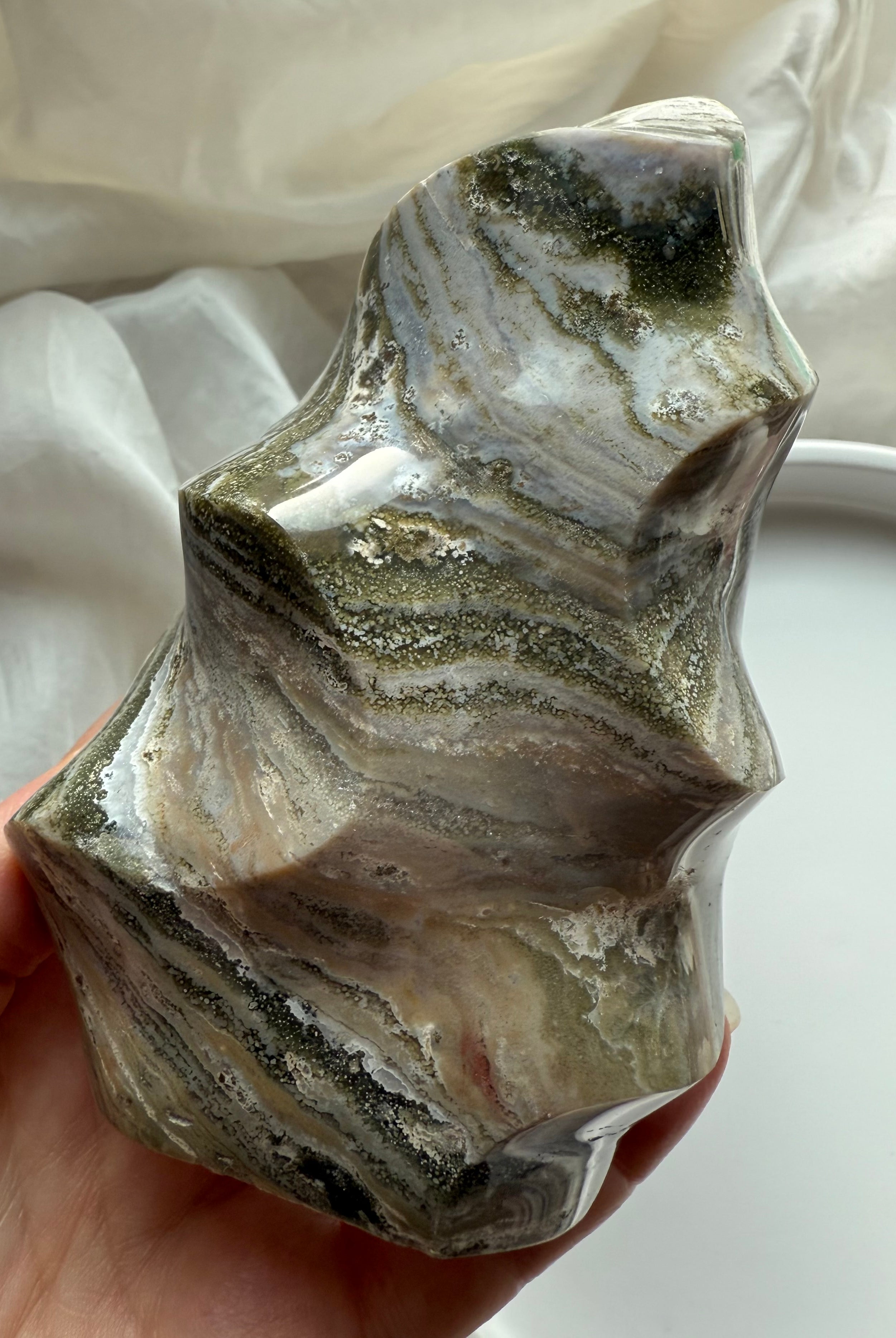 Hand-held view of Green Ocean Jasper flame highlighting its layered green, cream, and beige patterns in a glossy finish.