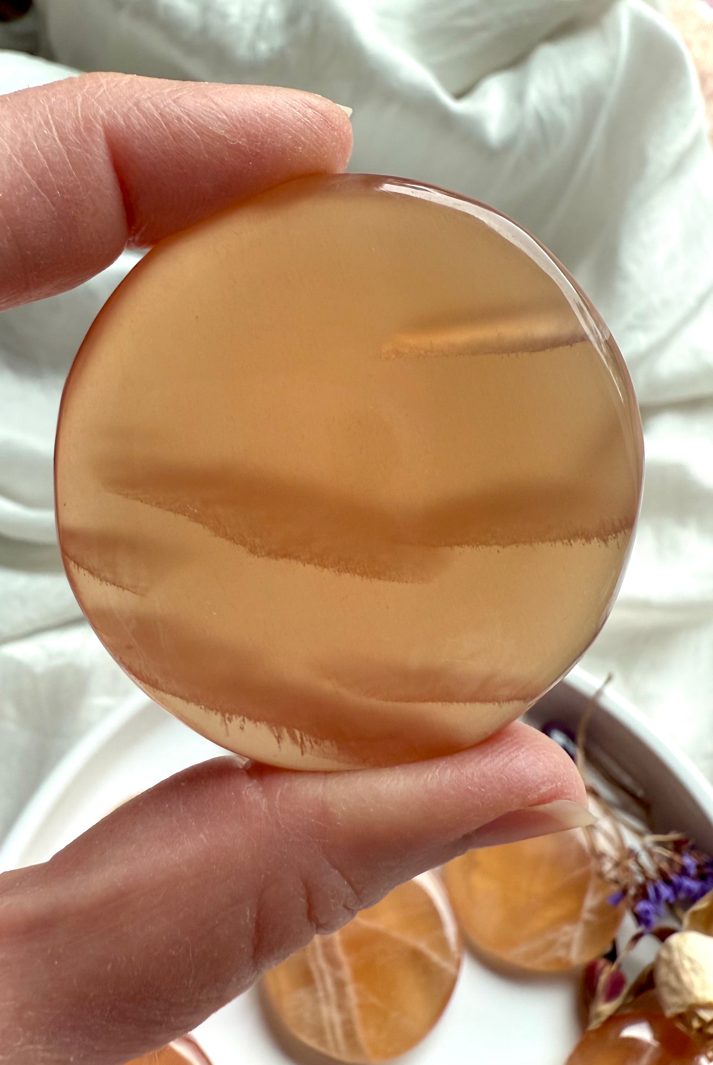 Closeup of a honey calcite meditation stone held between fingers, highlighting its soft golden hue and natural striations.
