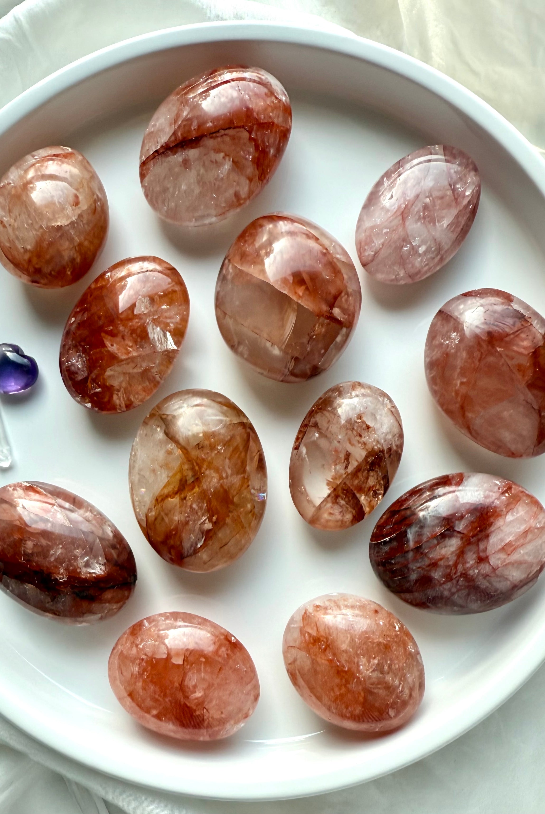 Assortment of polished Fire Quartz palm stones displayed in a white dish for energy healing rituals