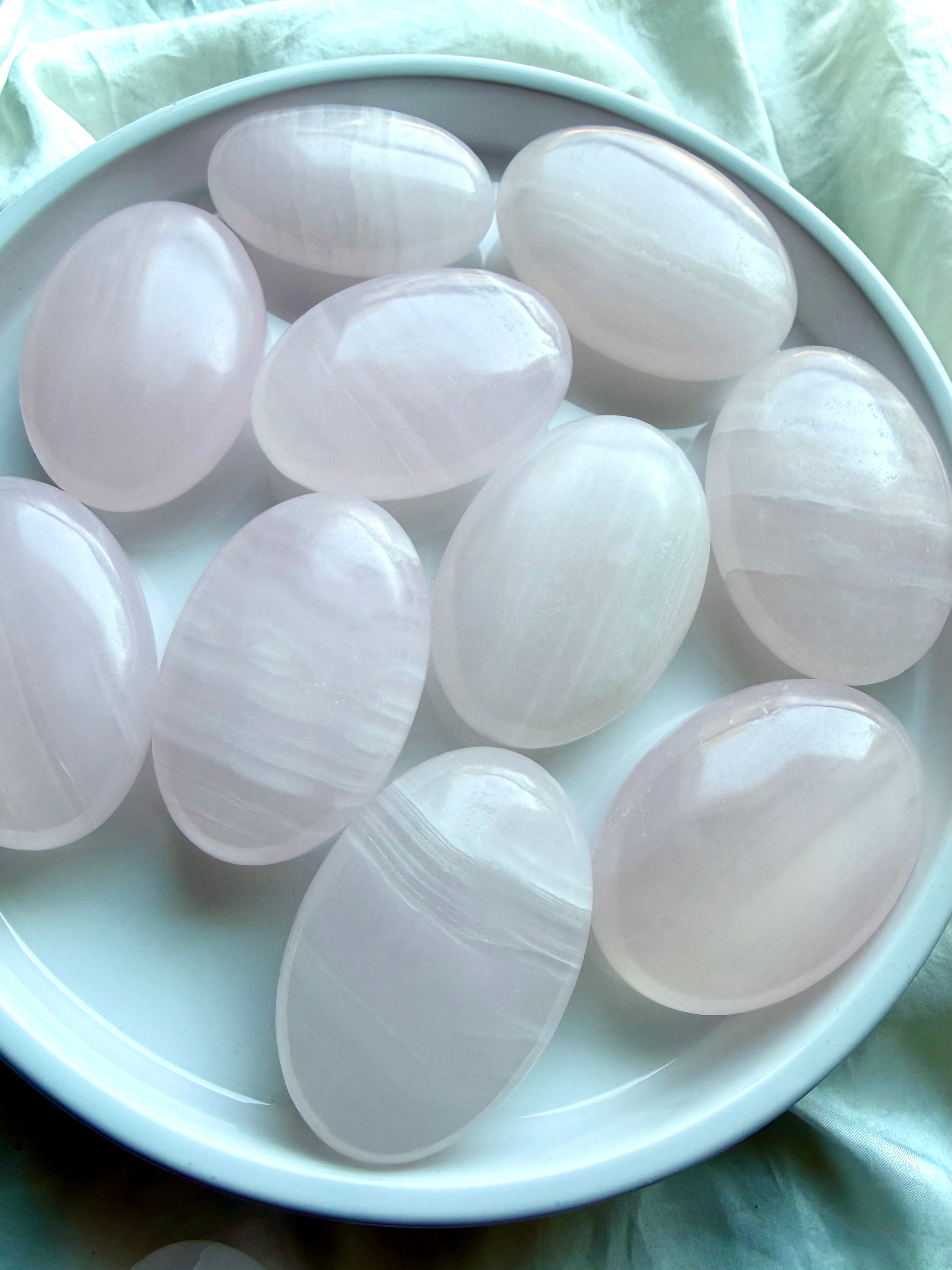 Assorted Mangano Calcite palm stones with polished finish, soft pink hues and natural banding