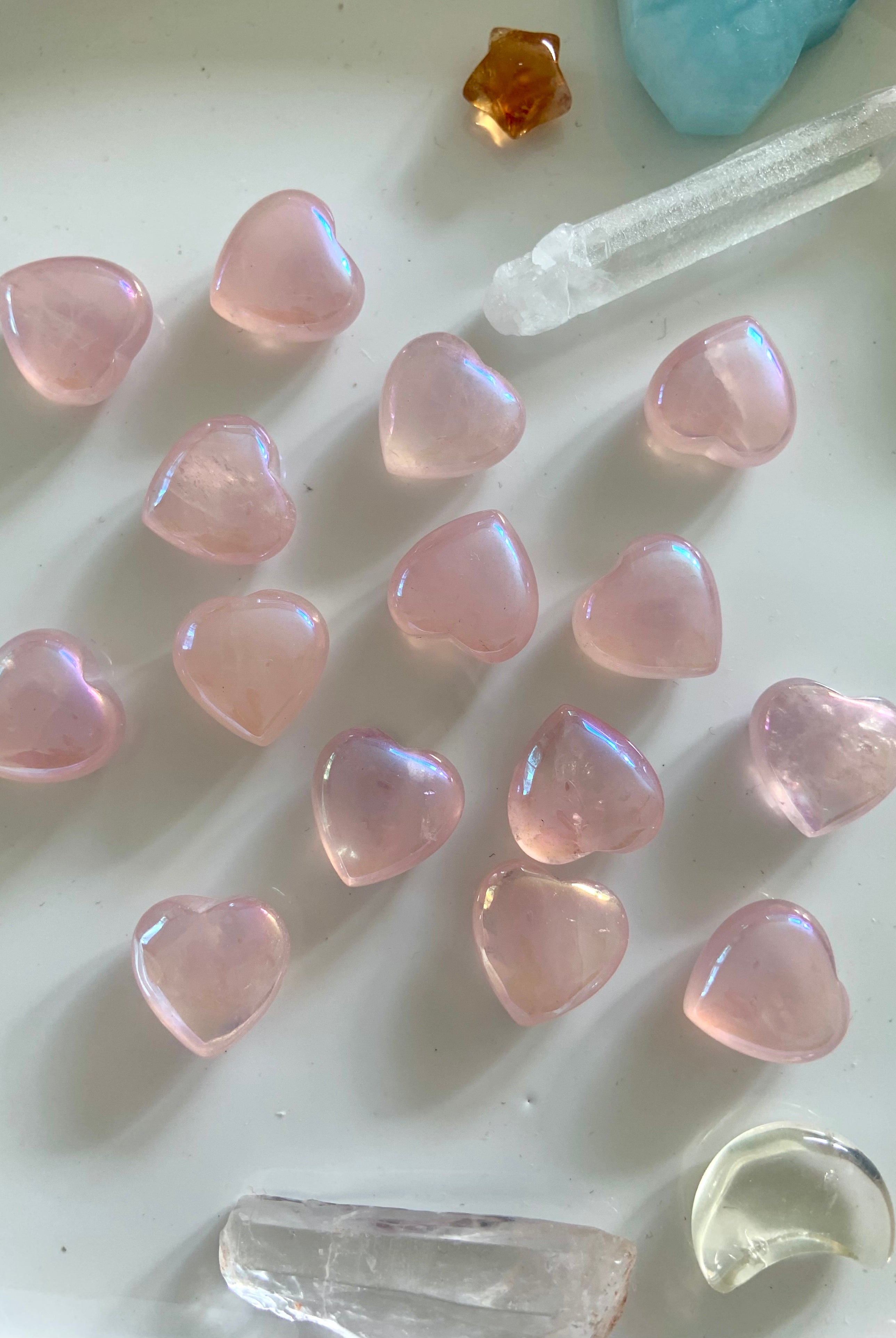 Flatlay of iridescent aura rose quartz hearts with other crystals on a white background — radiant heart chakra stones for spiritual love & peace