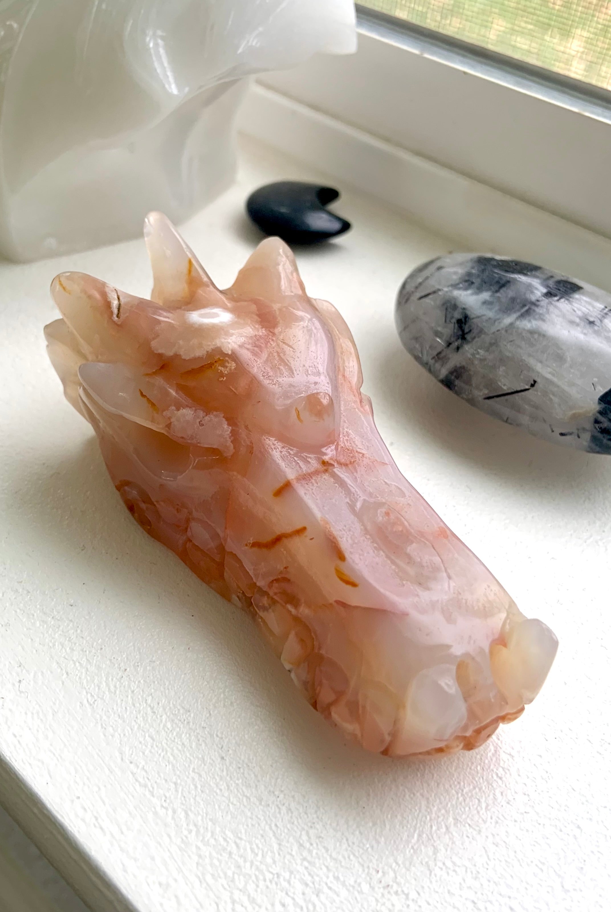 Carnelian Flower Agate Dragon Head Carving photographed in natura light on a windowsill with some other crystals