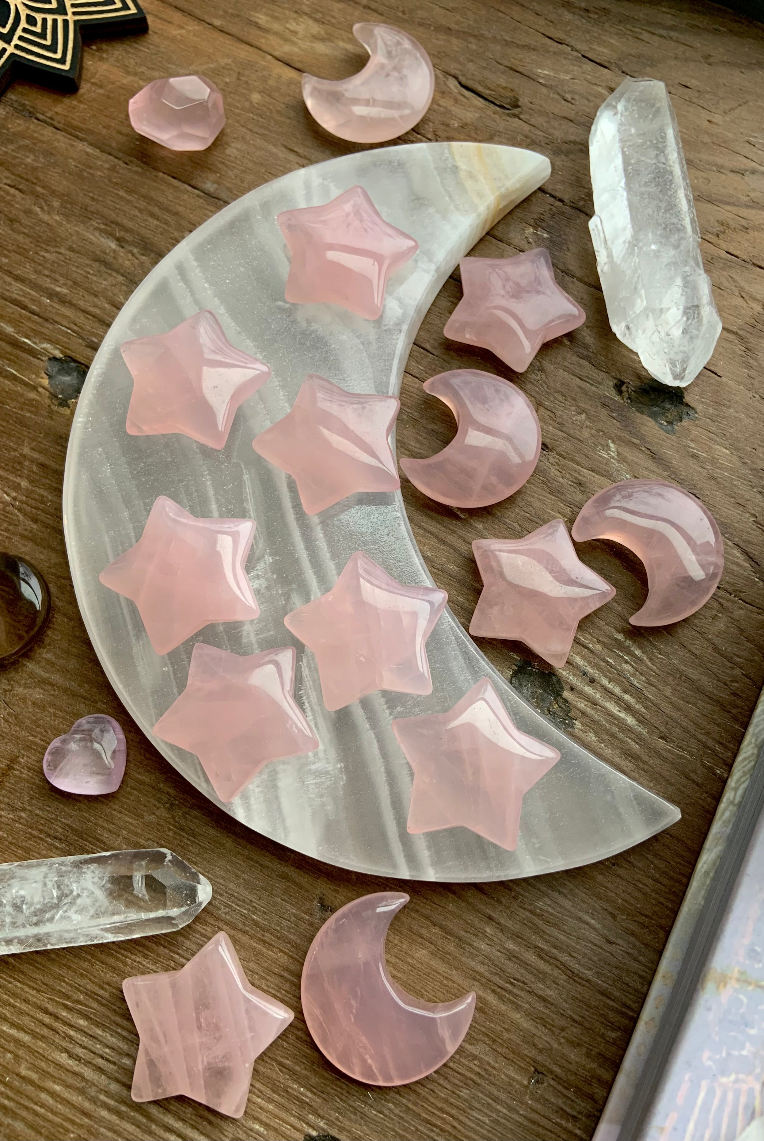 Small rose quartz moons and stars displayed on a white onyx moon plate with quartz points, photographed on dark wood. Heart Chakra crystals for peace, love & calm.
