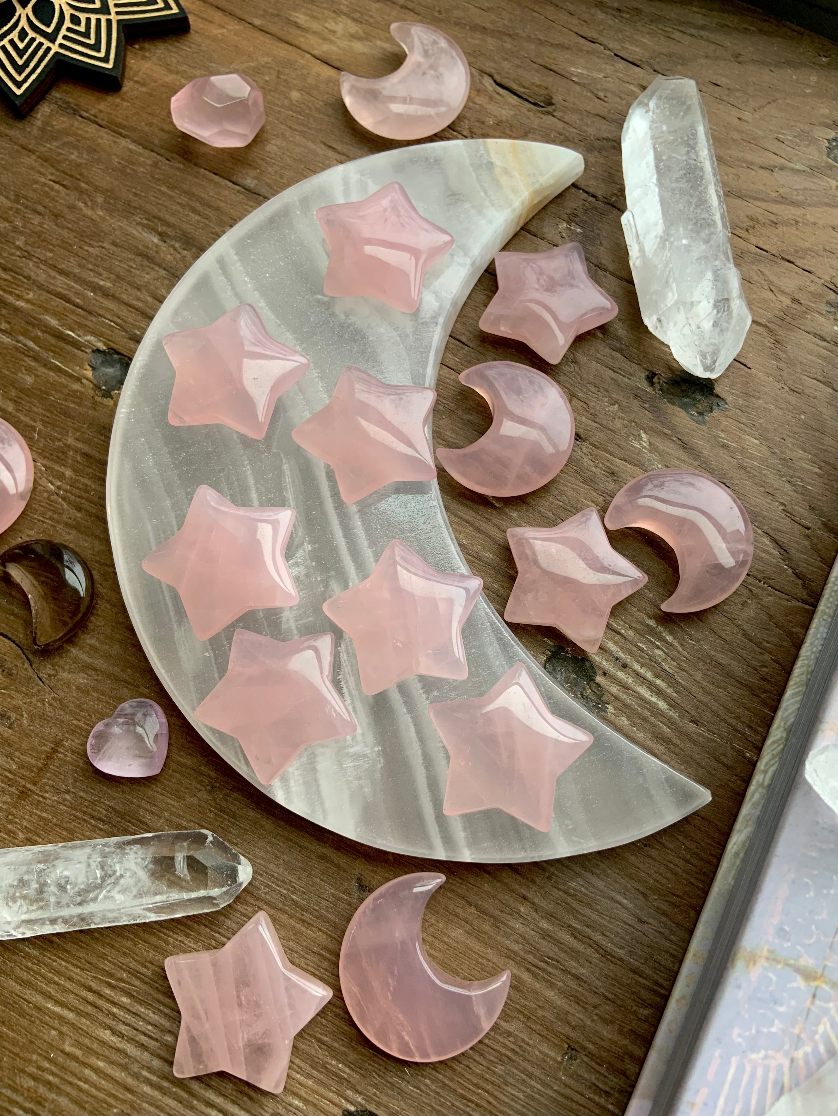 Small rose quartz moons and stars displayed on a white onyx moon plate with quartz points, photographed on dark wood. Heart Chakra crystals for peace, love & calm.