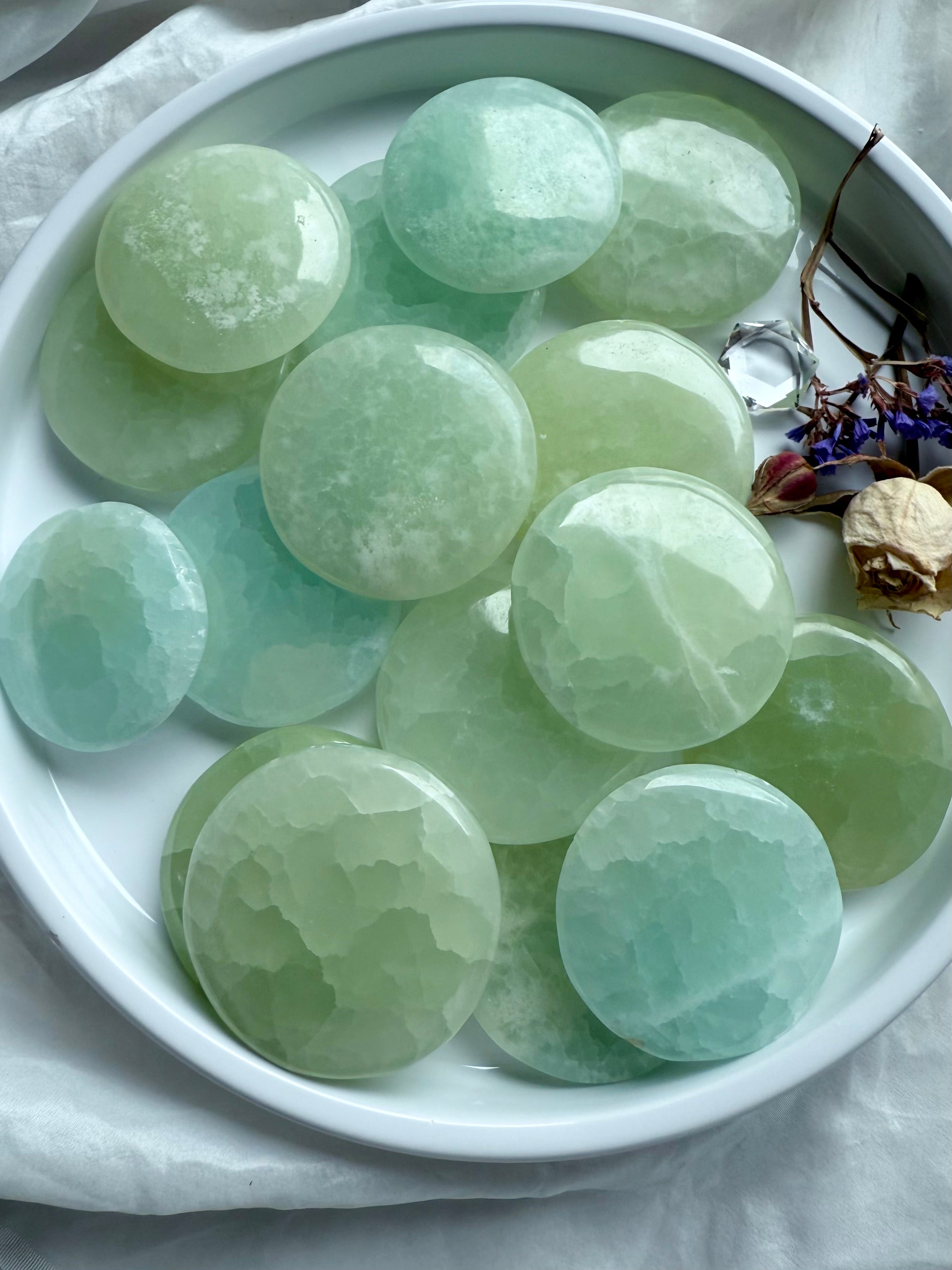 Polished Pistachio Calcite meditation stones in seafoam green tones arranged in a white dish with dried flowers – calming heart chakra crystals for emotional healing
