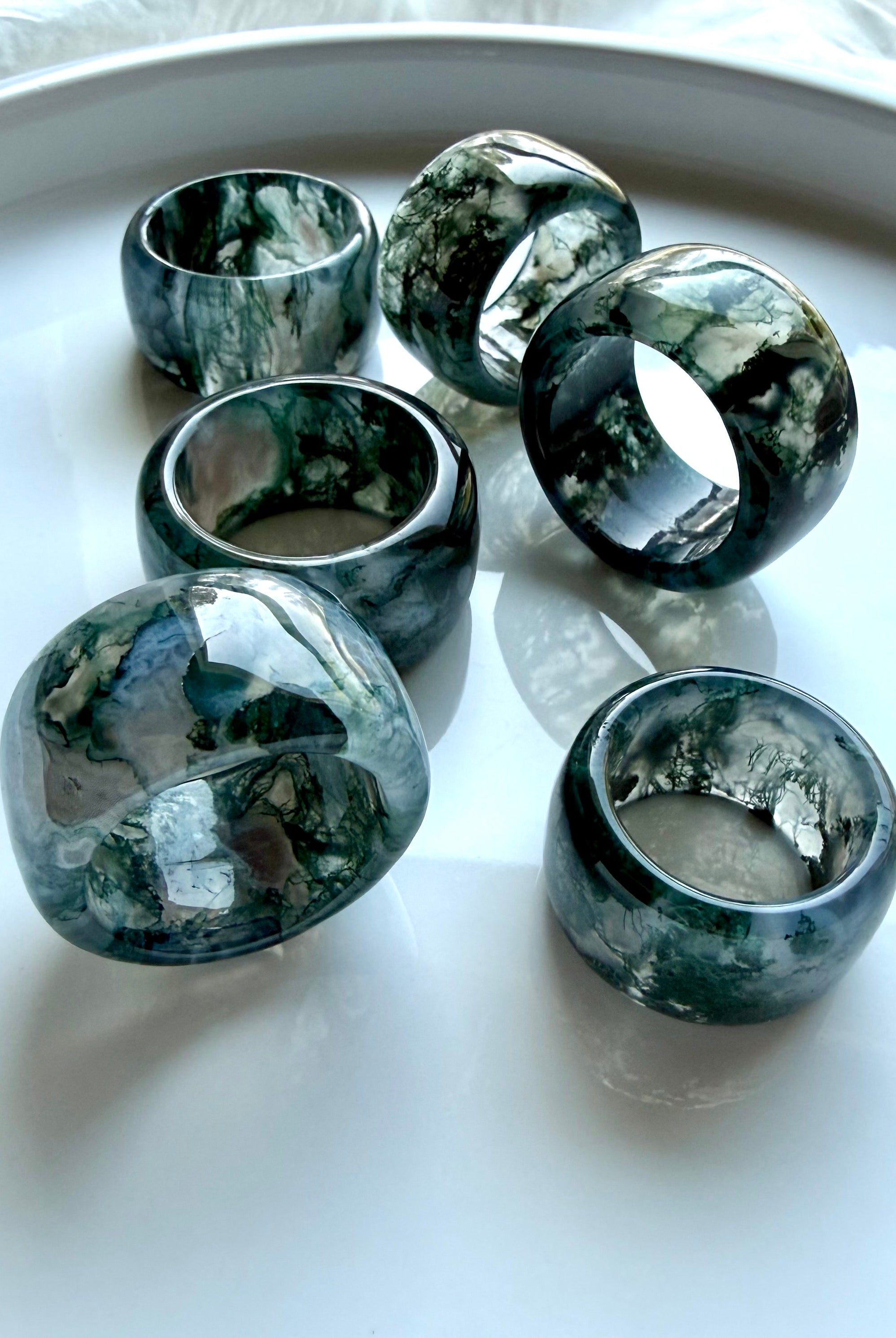 polished moss agate wide band rings grouped together on marble surface with translucent depth and organic natural patterns