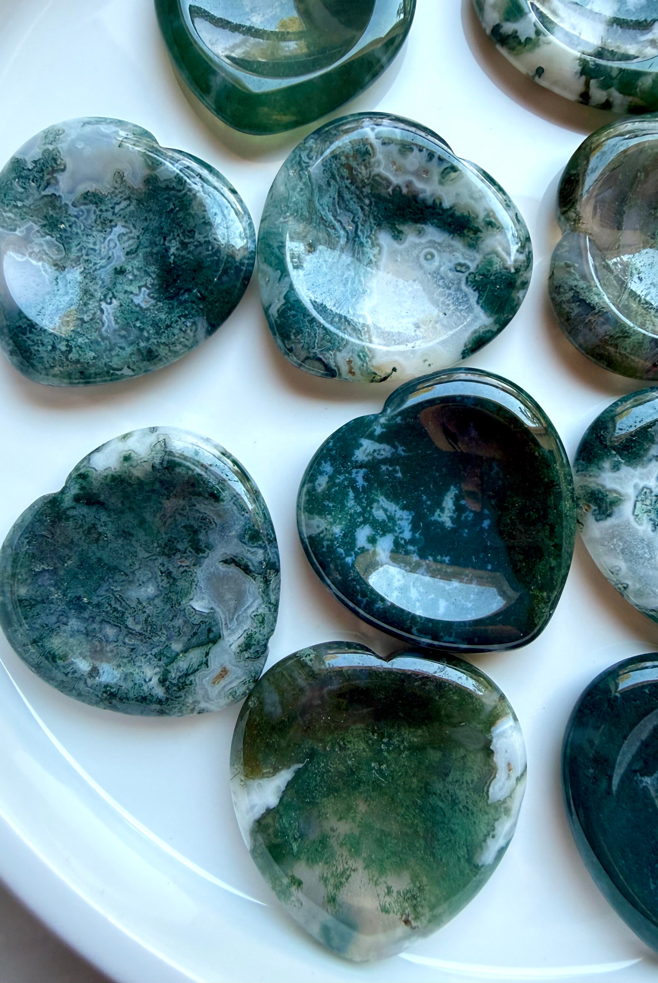 Assorted Moss Agate heart worry stones displayed on a white plate with natural moss patterns and polished finish