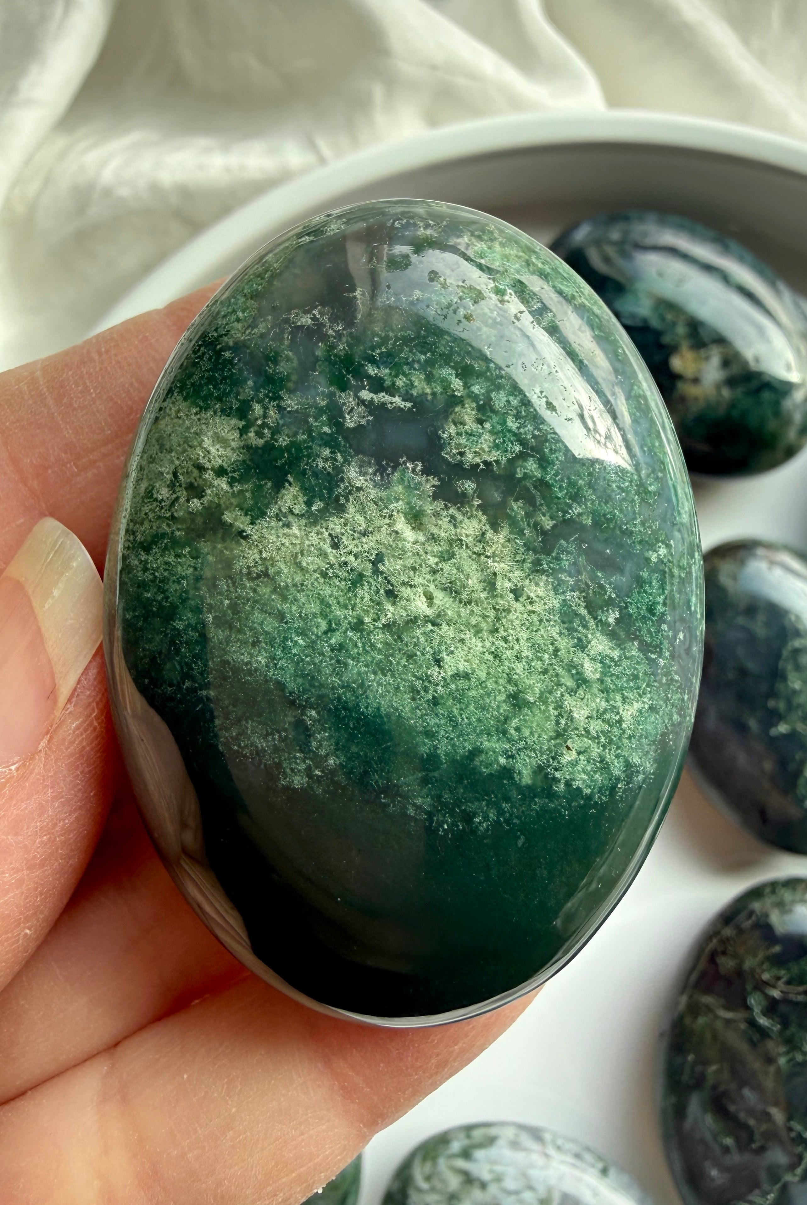 Close-up of moss agate palm stone in hand with translucent green inclusions, grounding stone for meditation and stress relief