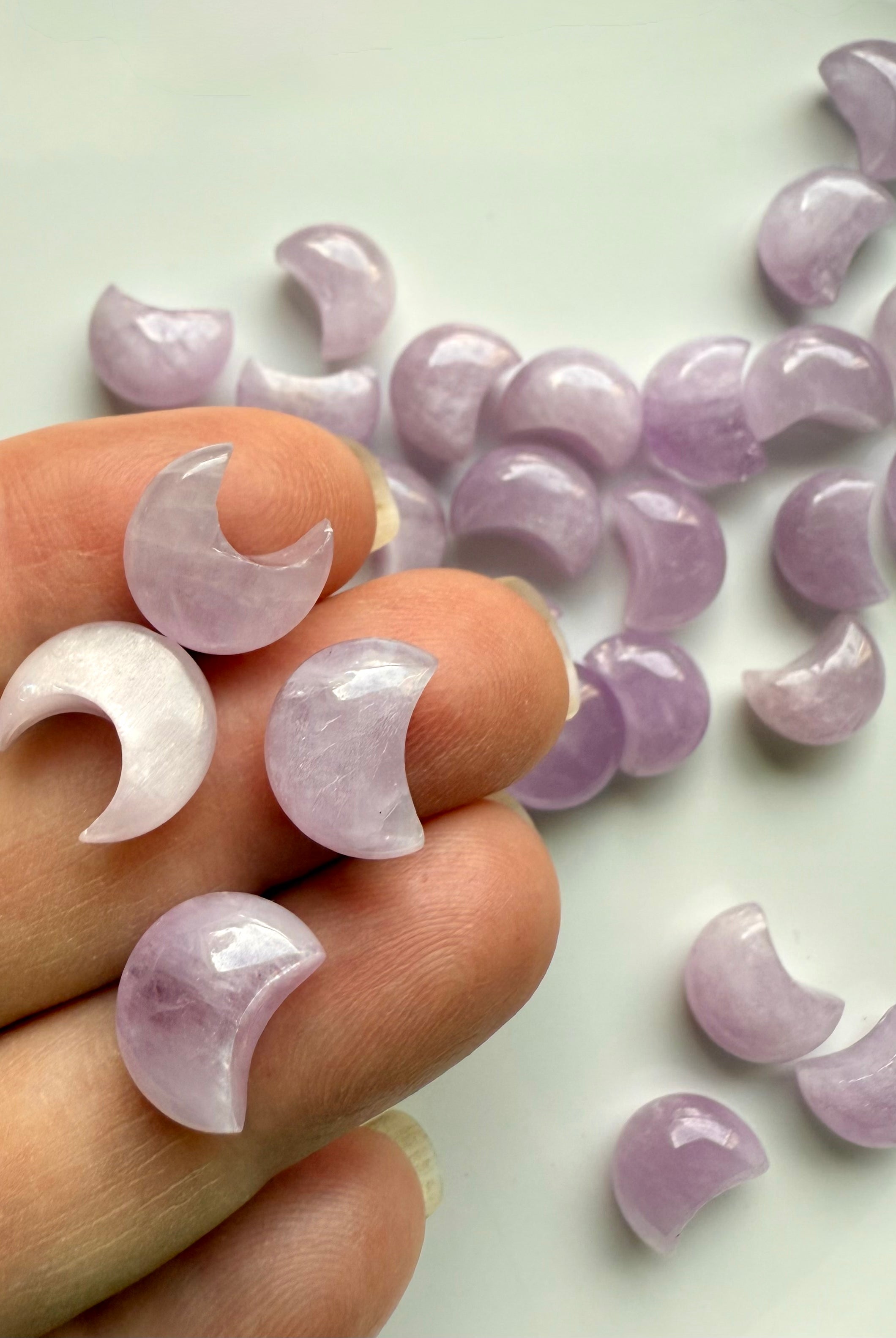 Closeup of mini Pink Kunzite moon carvings on fingertips — heart chakra crystals for love, compassion & peace.