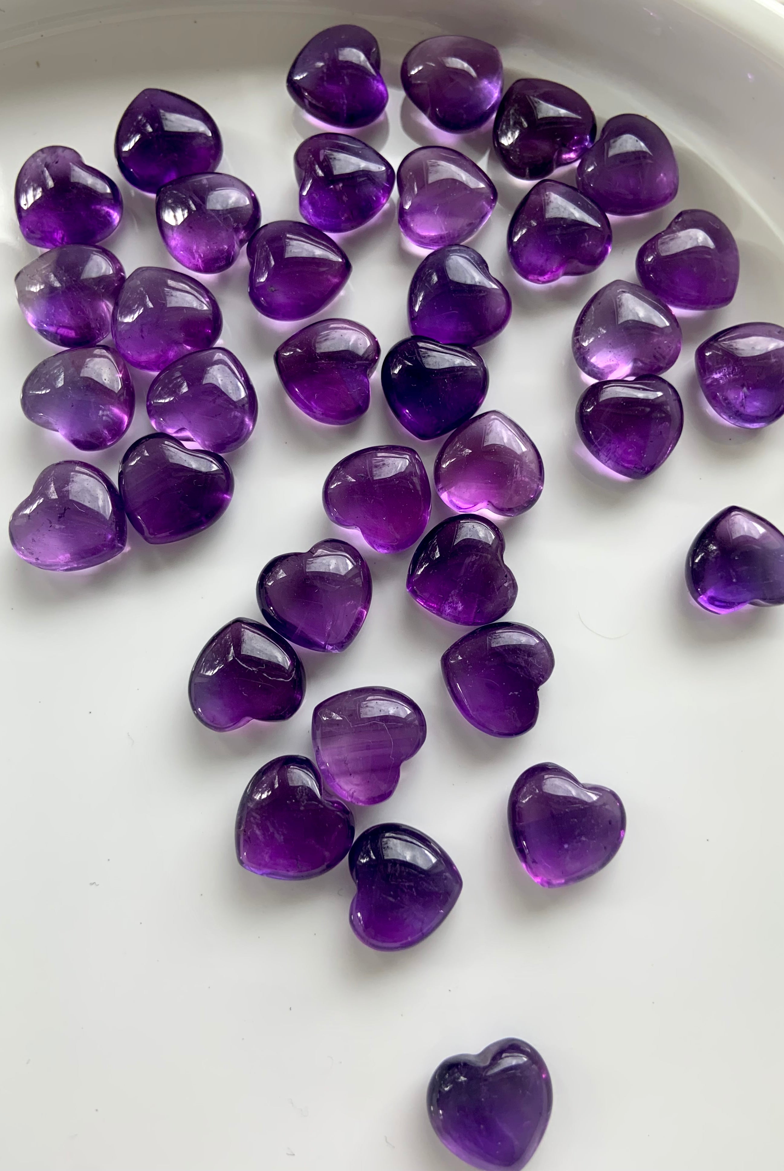 Wide angle view of scattered Amethyst hearts on a white plate — radiant mini crystals for divine guidance