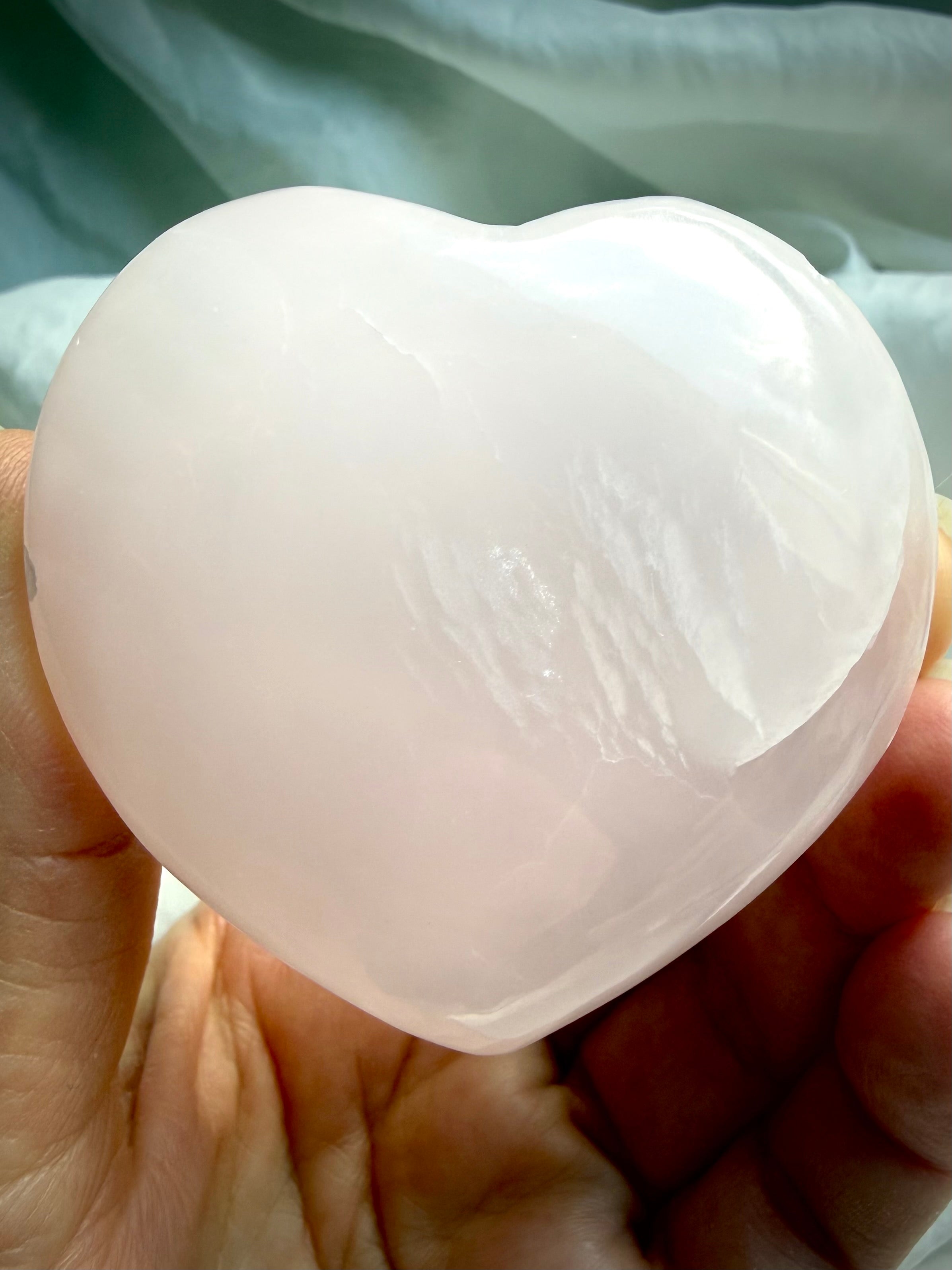 One of a kind Mangano Calcite heart carving displayed on marble with soft translucent pink glow