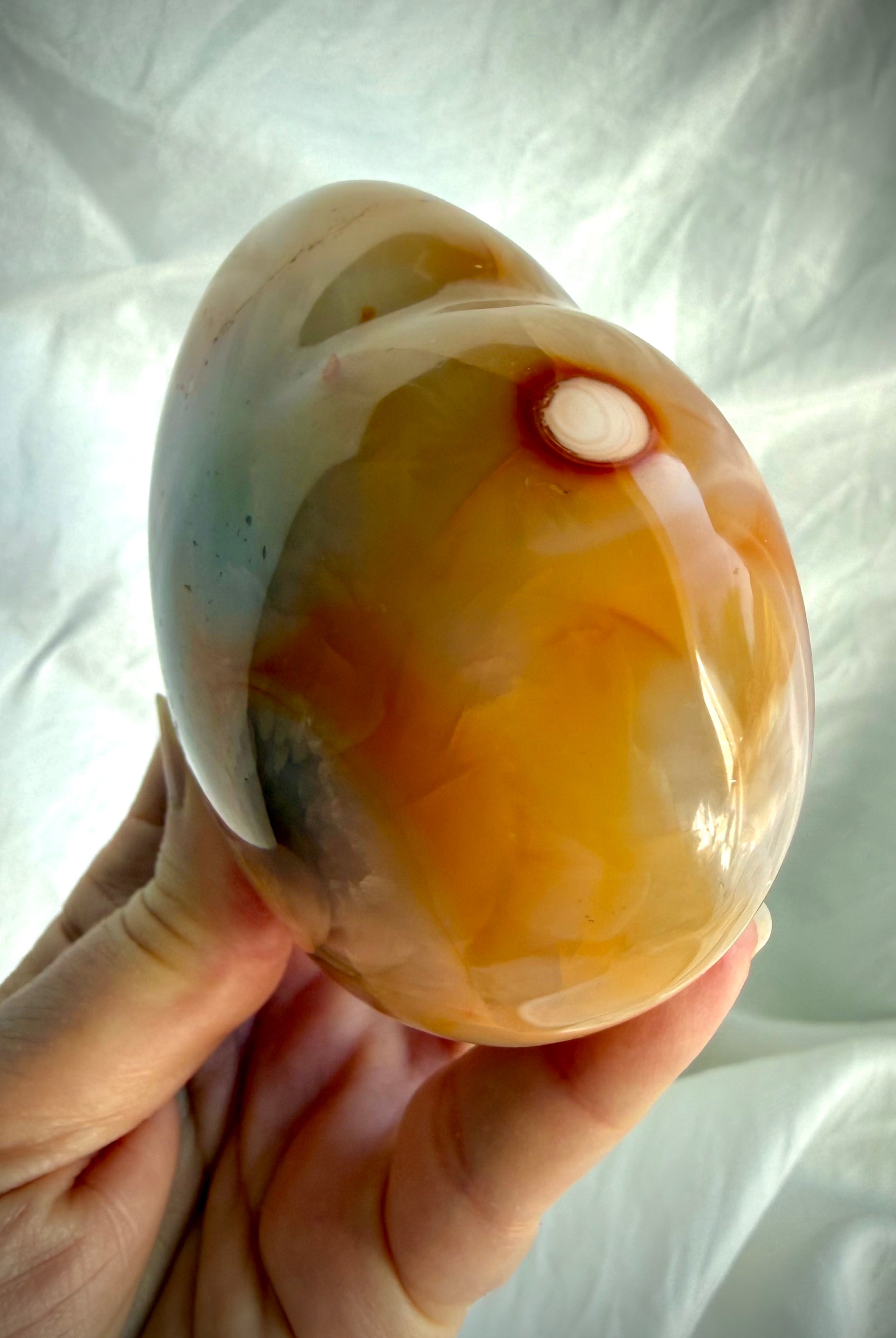 Side view of polished Carnelian heart crystal highlighting thickness, curved profile and natural orbicular pattern
