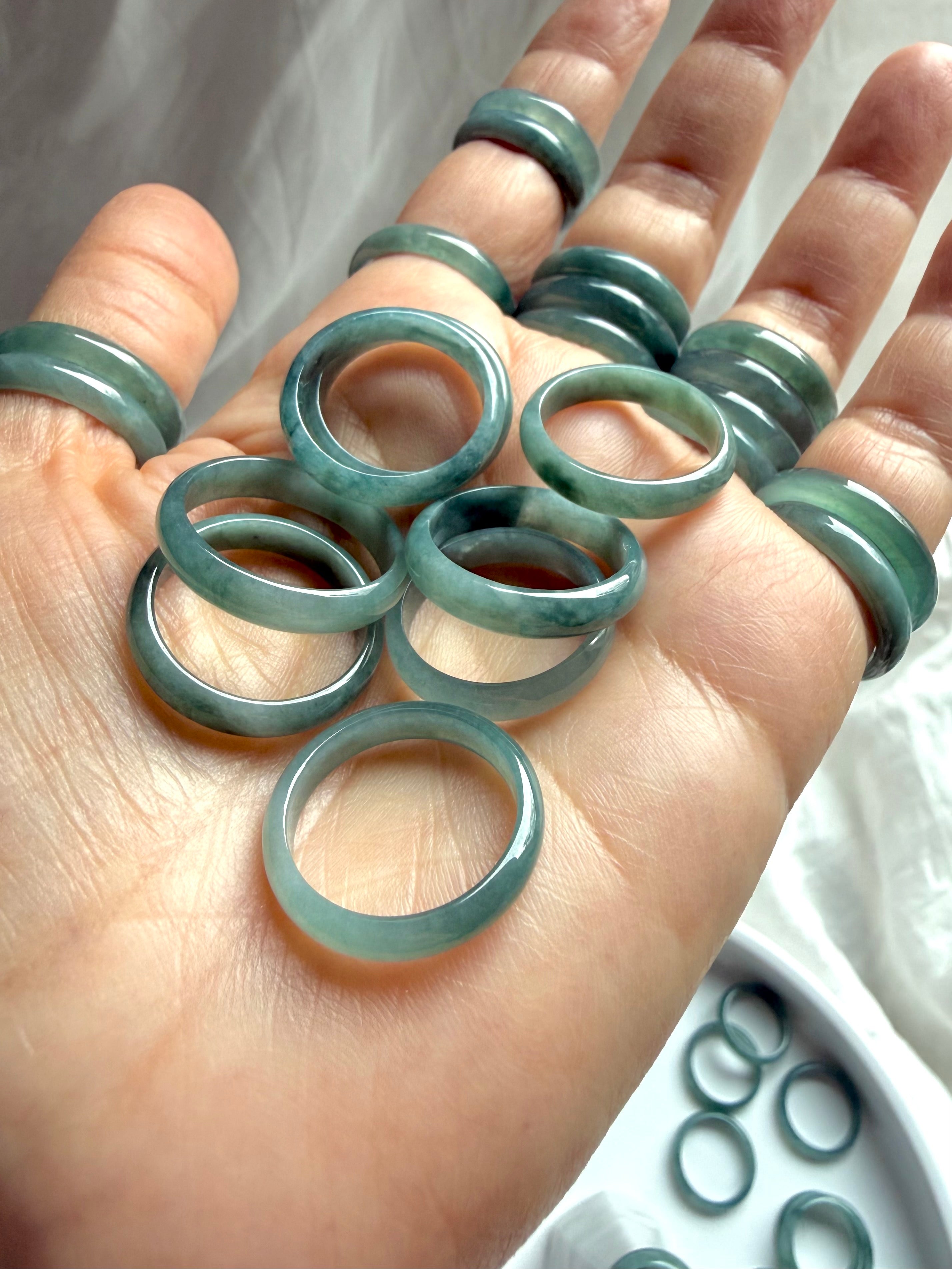 Multiple rounded Blue Water jadeite rings shown in hand, smooth natural jade bands