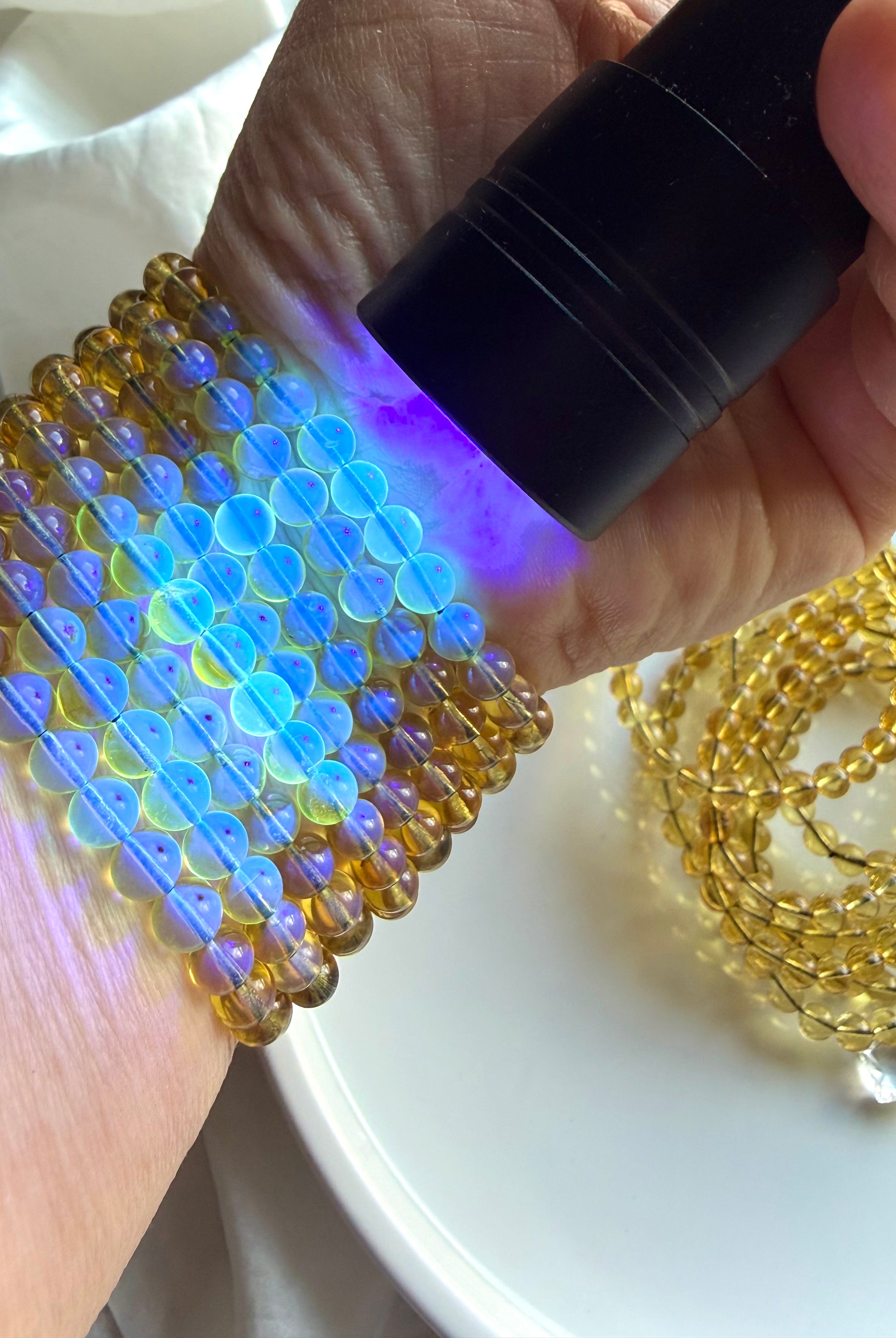 Blue amber crystal bead bracelet glowing under UV flashlight – Indonesian UV reactive amber