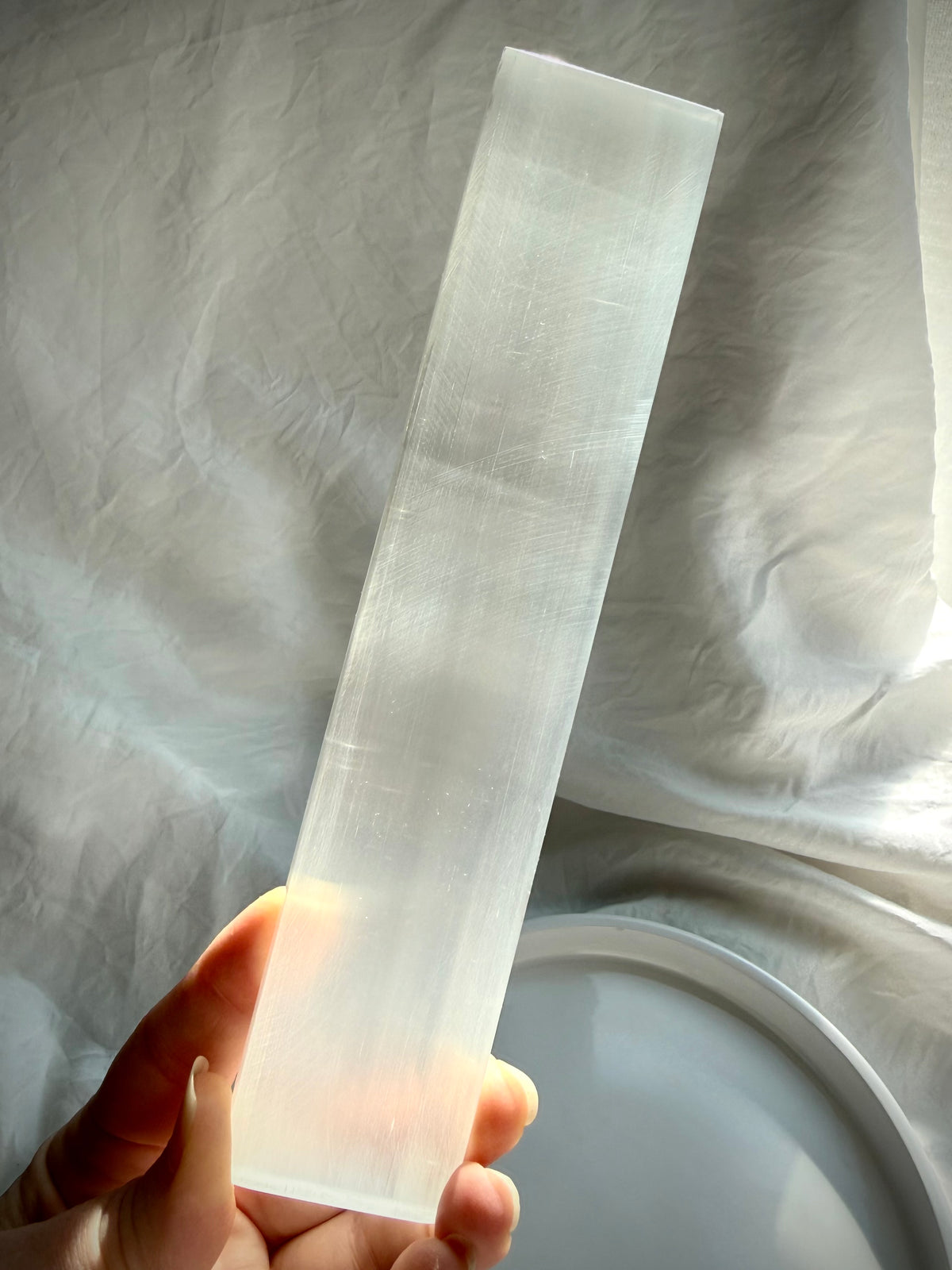 Selenite charging bar held in hand, showing translucent white Satin Spar crystal with a luminous glow for energy clearing and cleansing