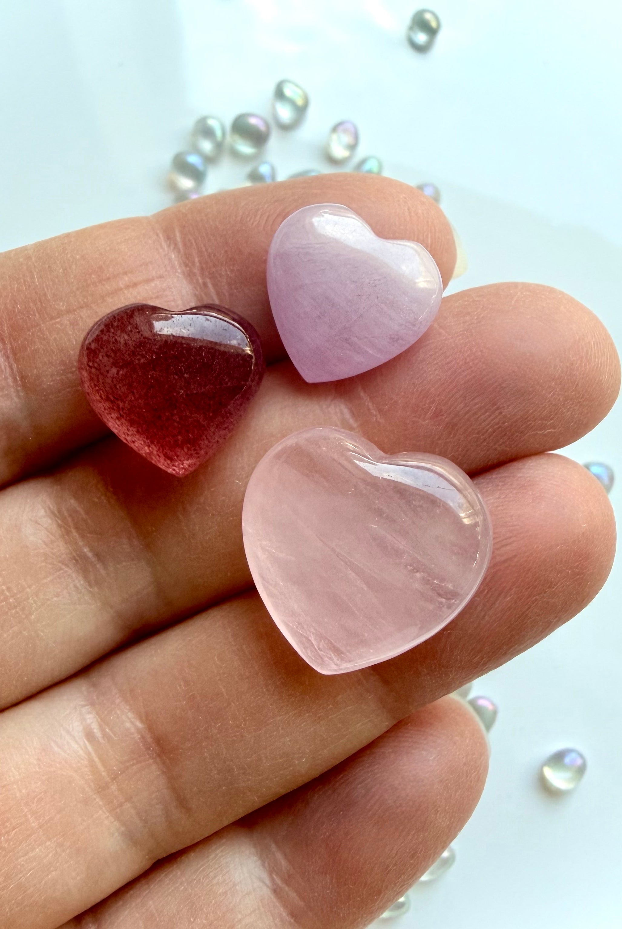 Mini crystal heart trio in hand showing size of rose quartz, strawberry quartz, and kunzite pocket stones