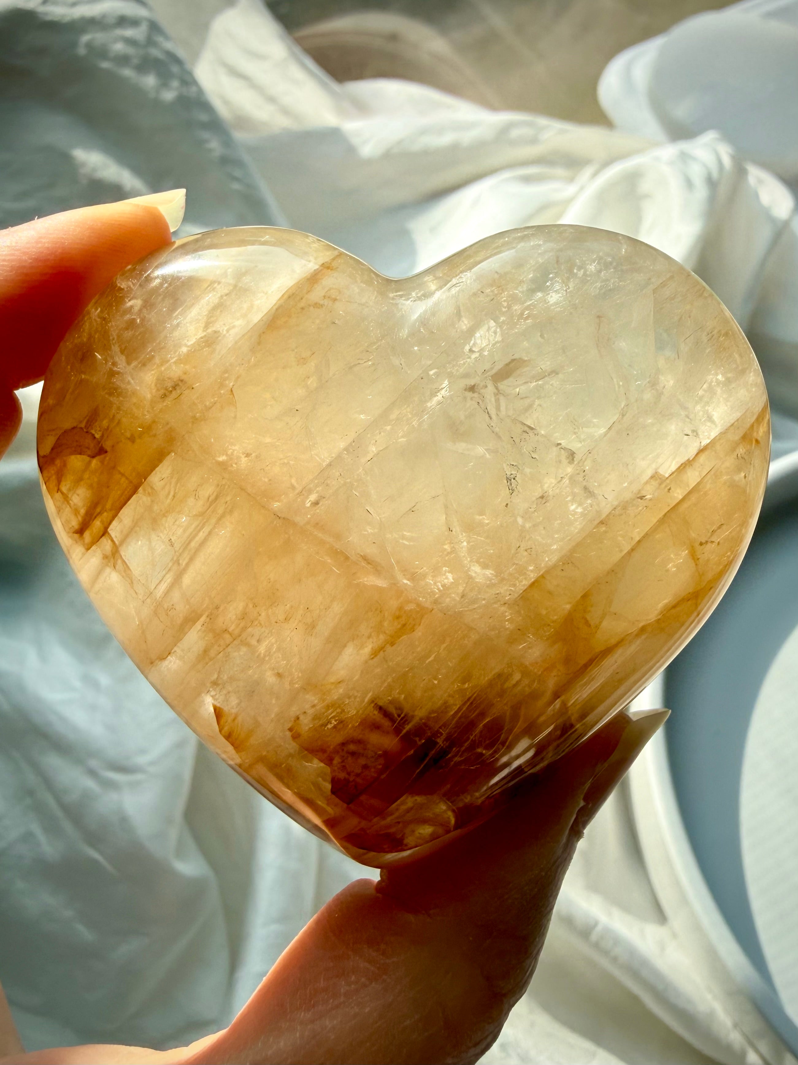Hand holding one of a kind Golden Healer heart crystal glowing with honey gold tones for empowerment and aligned action