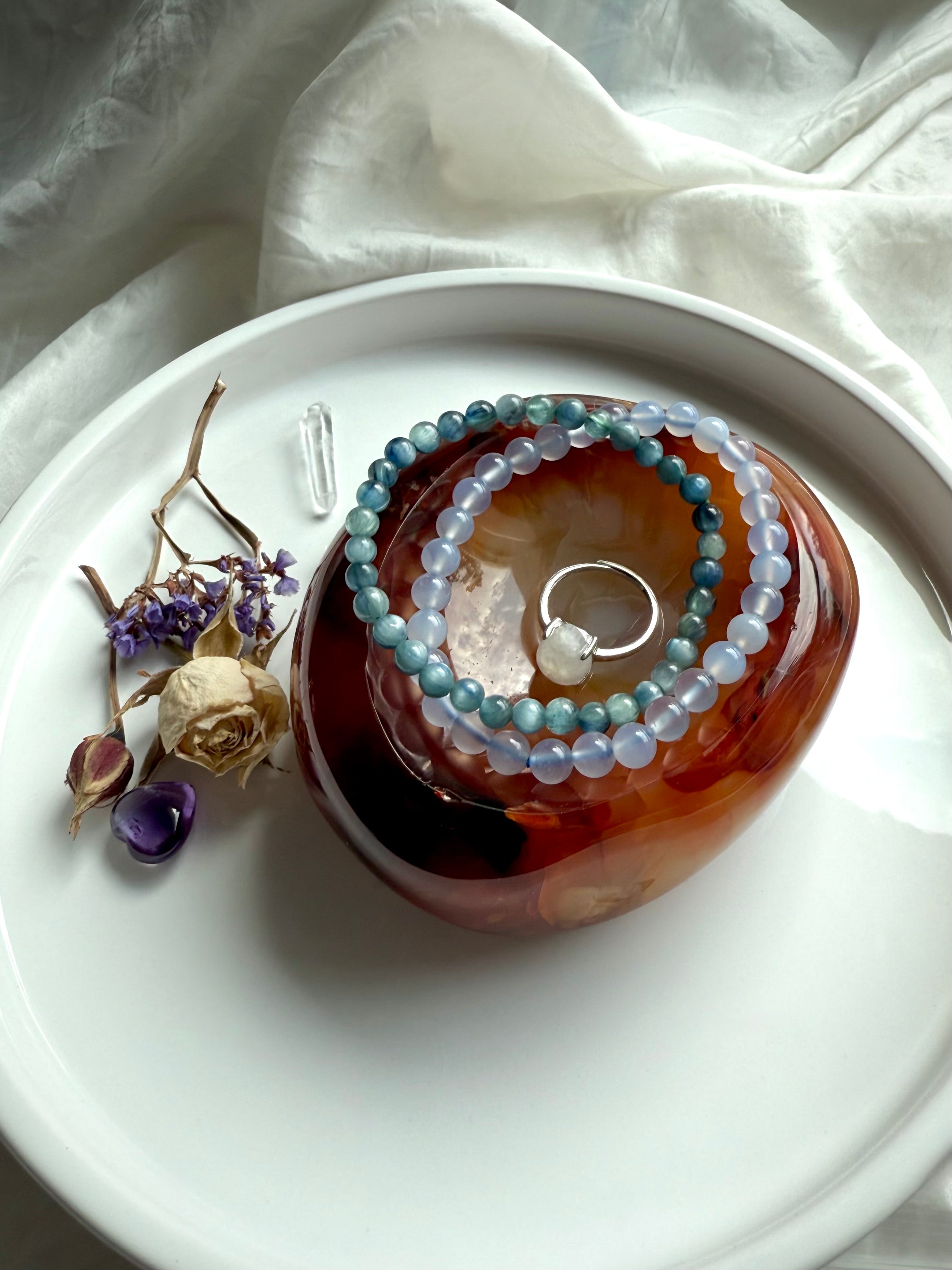 Carnelian crystal bowl used as a jewelry holder, holding gemstone bracelets and a ring, styled with dried flowers.