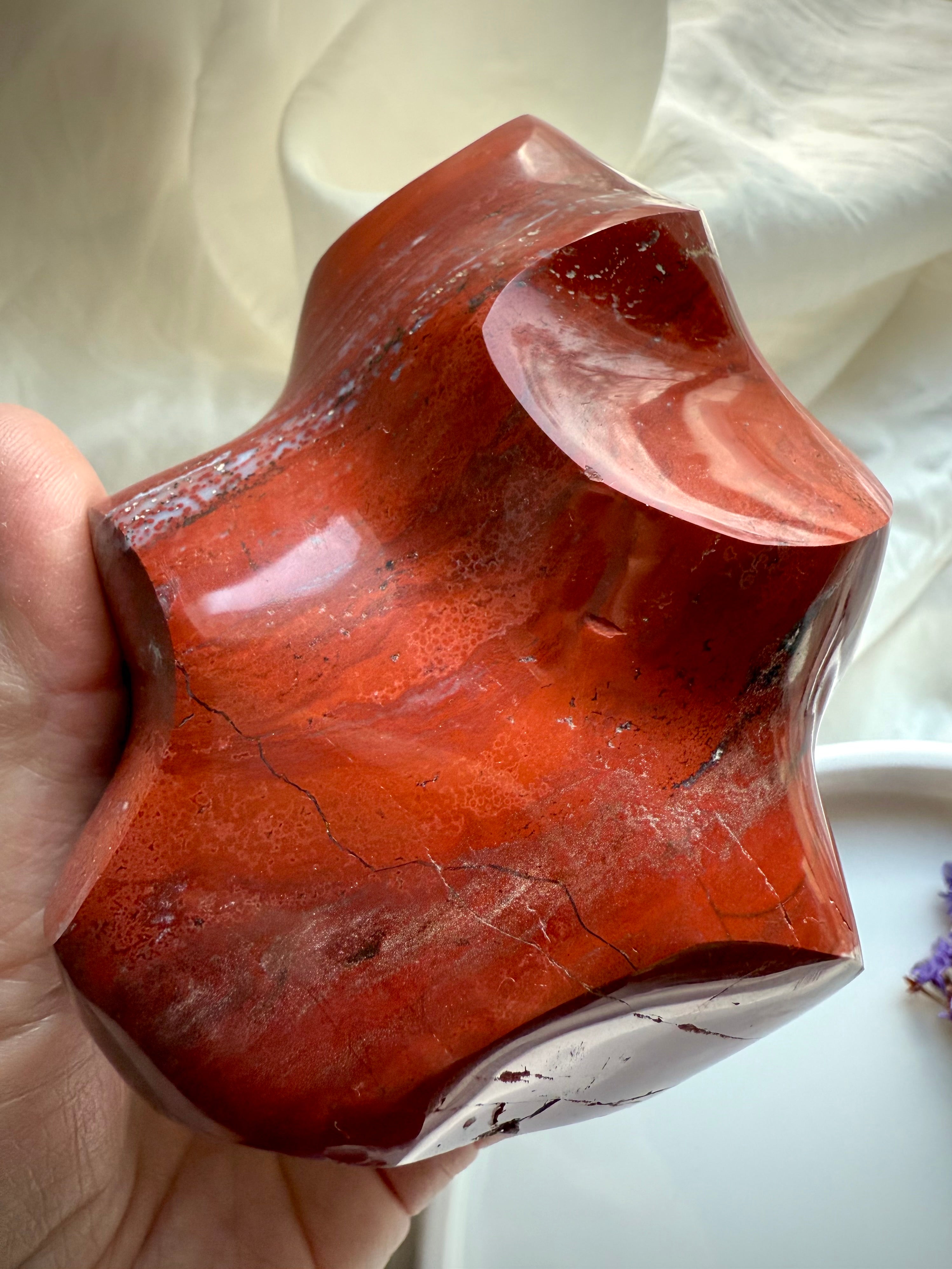 Hand-held Red Ocean Jasper flame with deep red layers, grounding Root Chakra energy, and swirling natural textures.