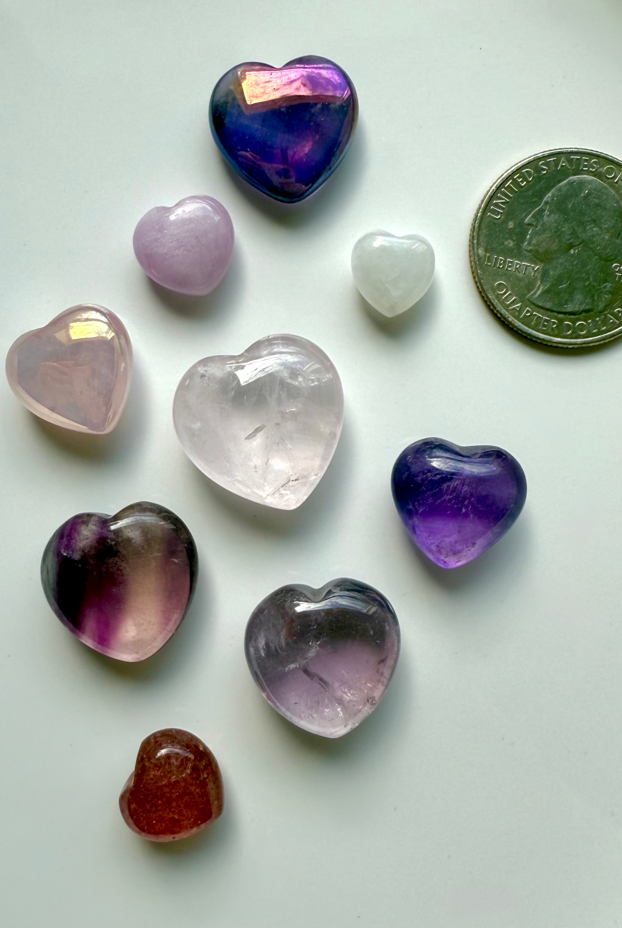 Close-up of pink and purple mini crystal hearts on white background with a quarter for size comparison, premium gemstone carvings.